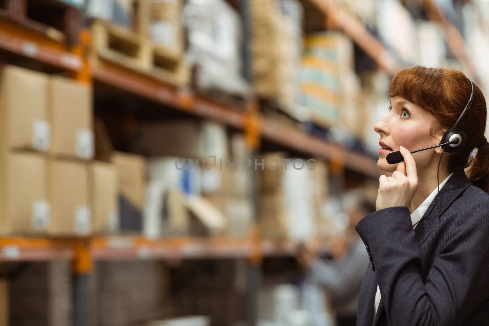 Pretty businesswoman speaking in a headset in a large warehouse