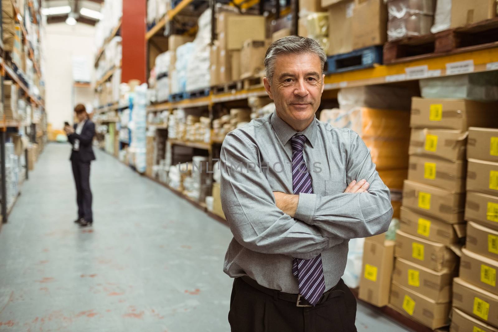 Smiling male manager with arms crossed in a large warehouse