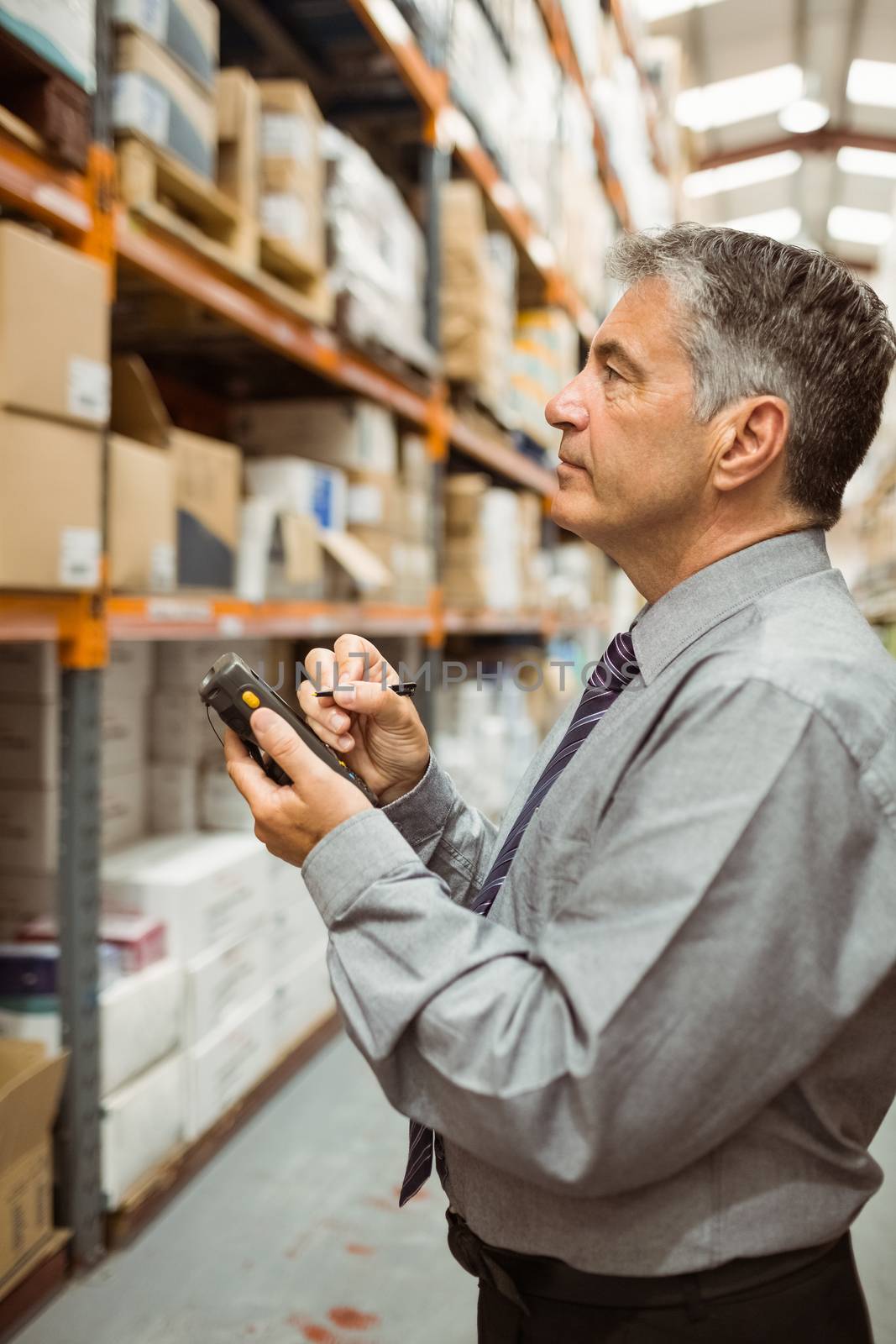 Focused male manager using handheld in a large warehouse