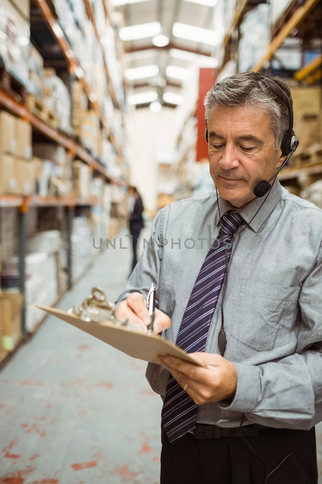 Warehouse manager writing on clipboard in a large warehouse