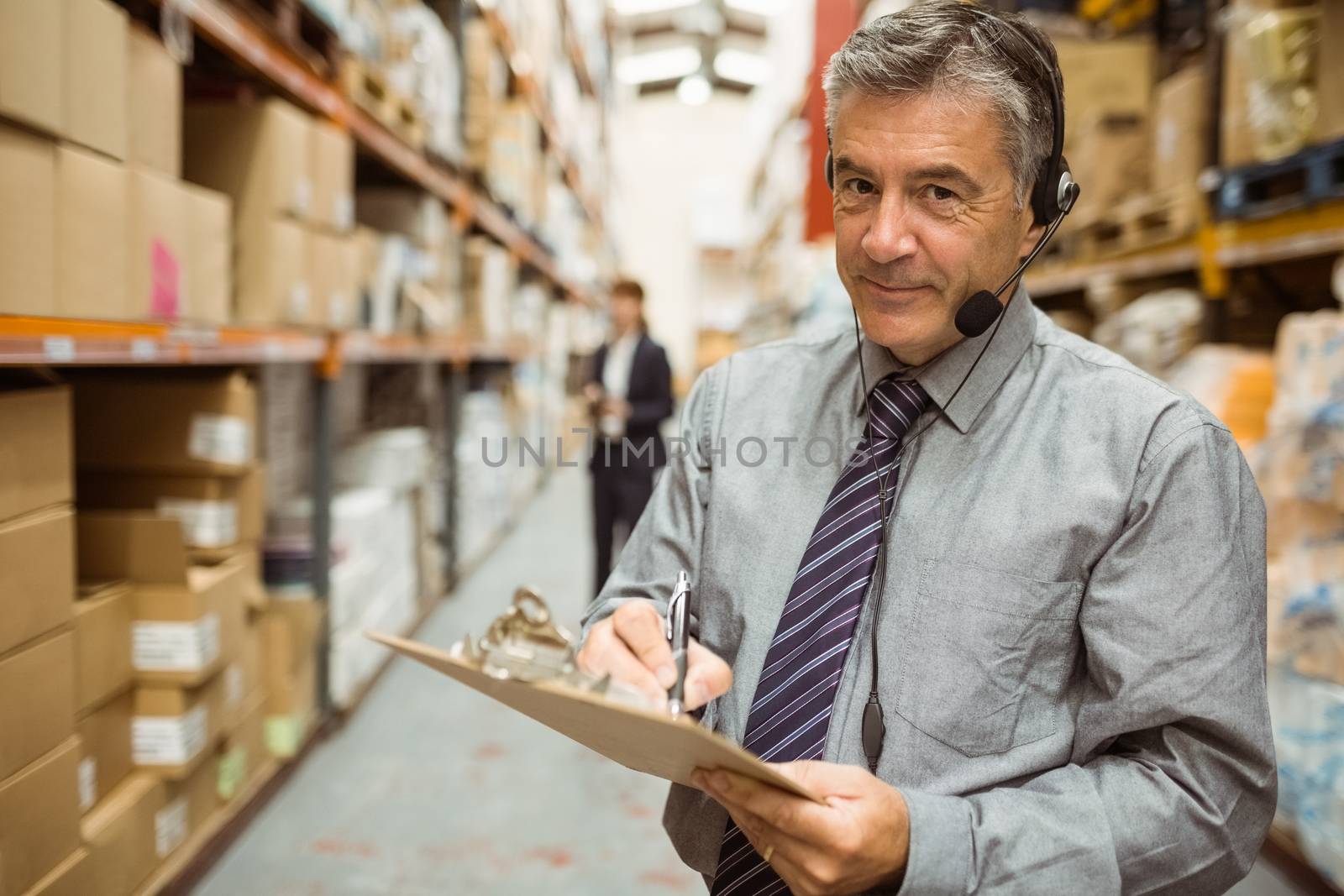 Warehouse manager writing on clipboard in a large warehouse