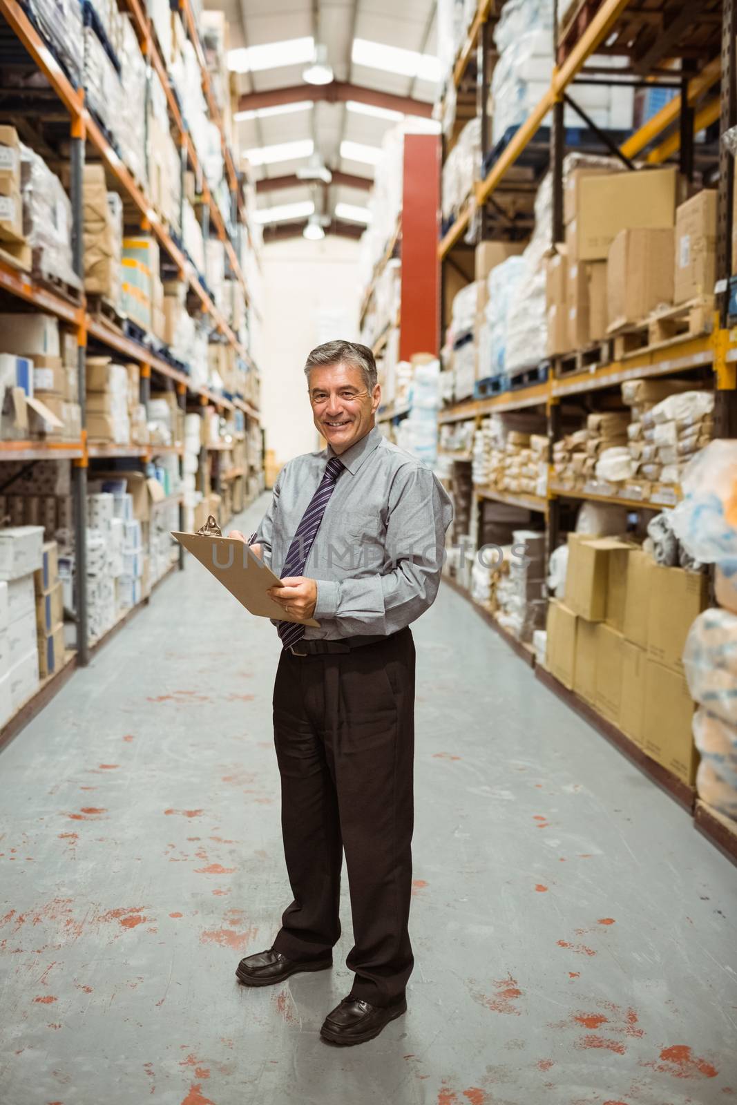 Smiling warehouse manager writing on clipboard in a large warehouse