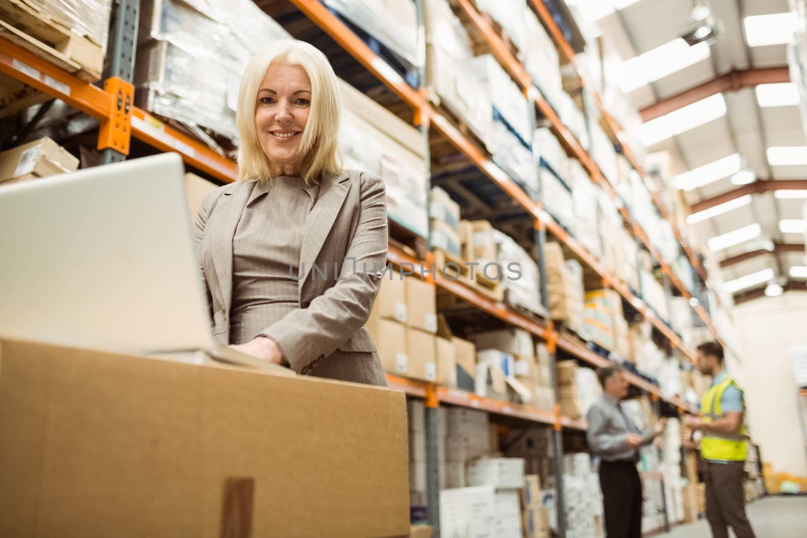 Smiling warehouse manager working on laptop in a large warehouse