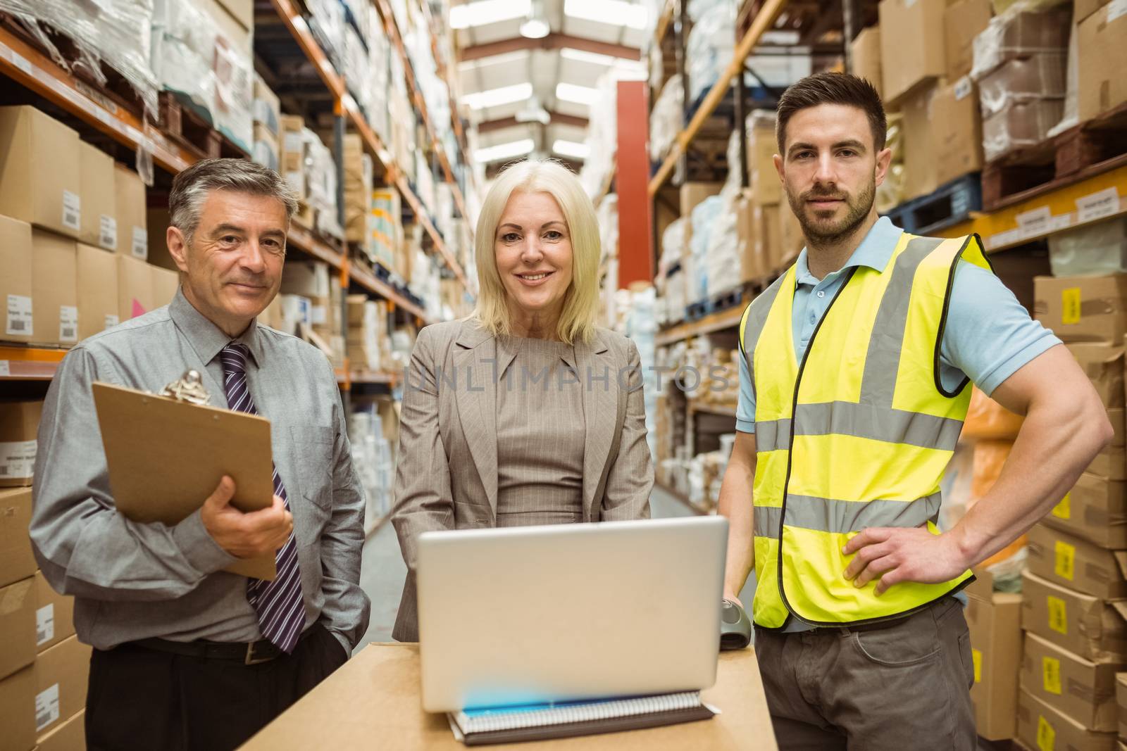 Smiling warehouse team working together on laptop in a large warehouse