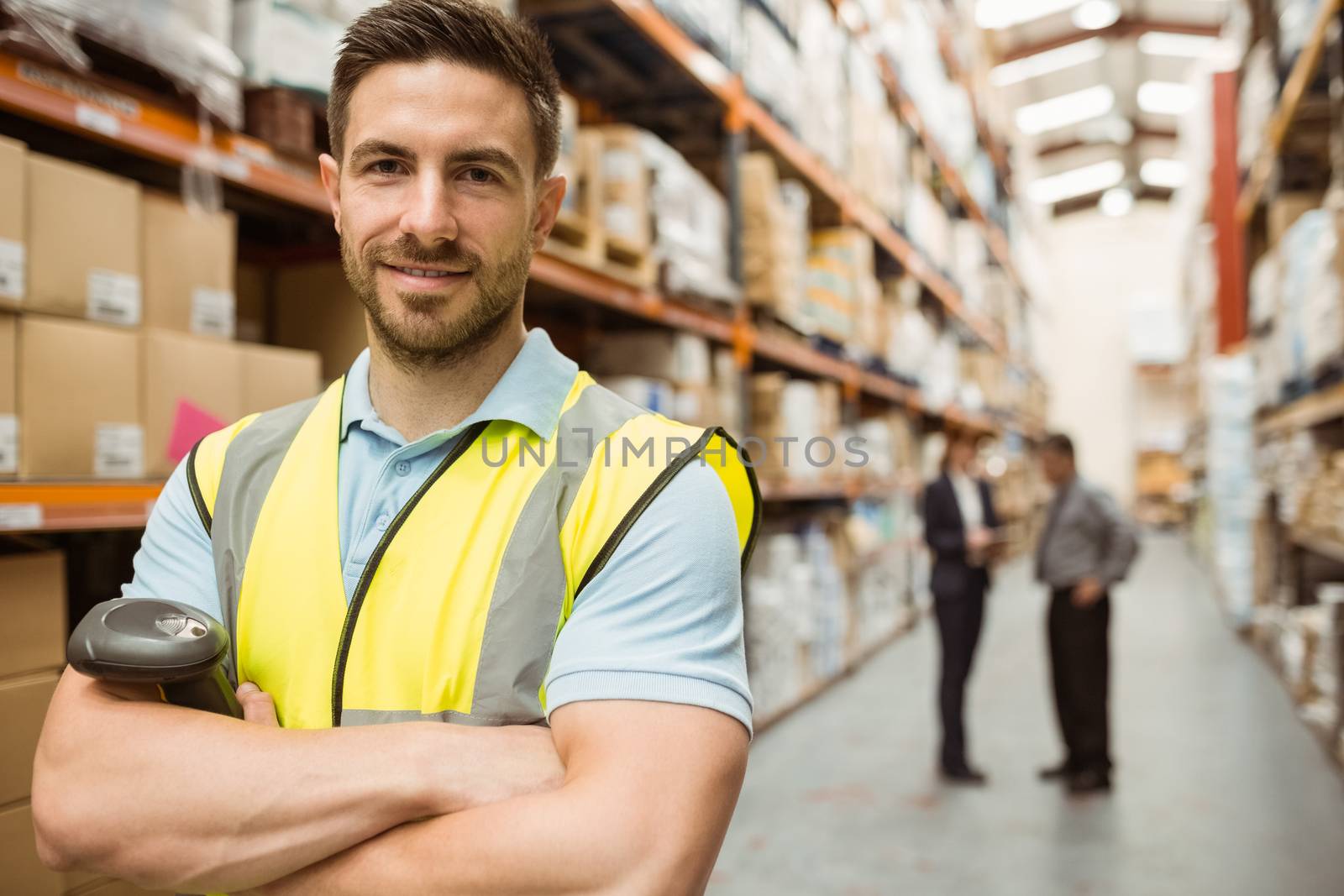 Smiling worker standing with arms crossed in a large warehouse