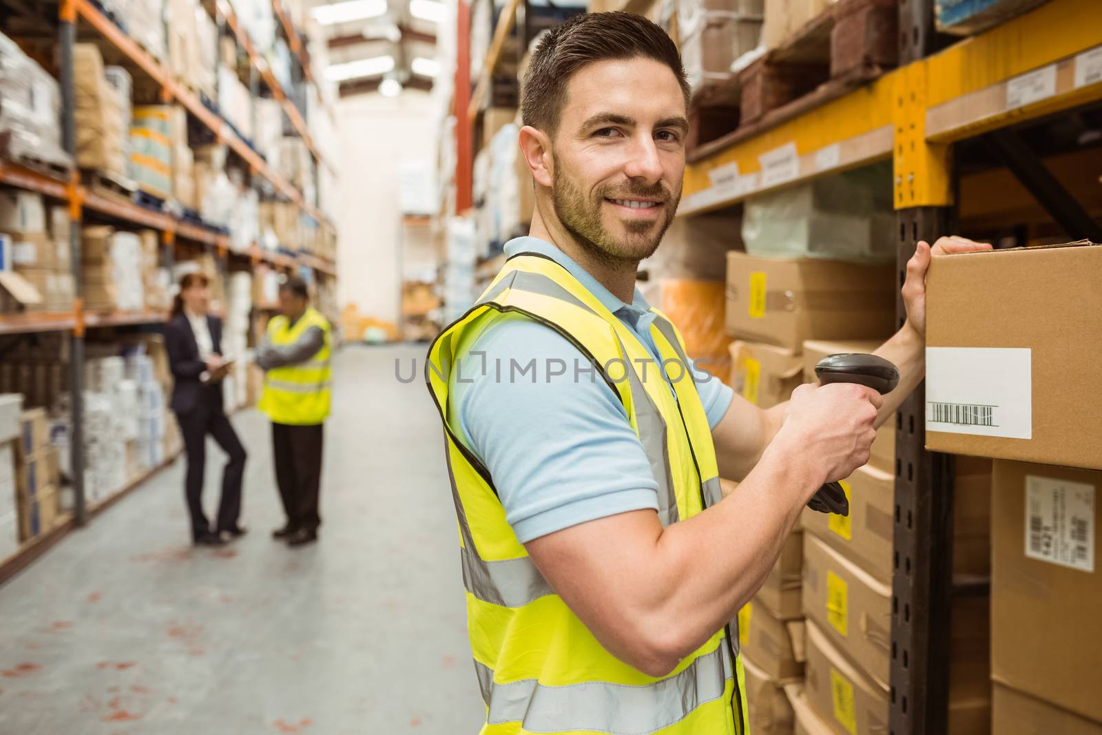 Warehouse worker scanning box while smiling at camera by Wavebreakmedia
