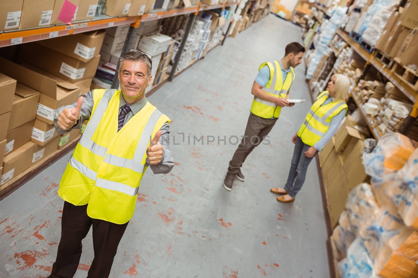 Warehouse manager smiling at camera showing thumbs up in a large warehouse