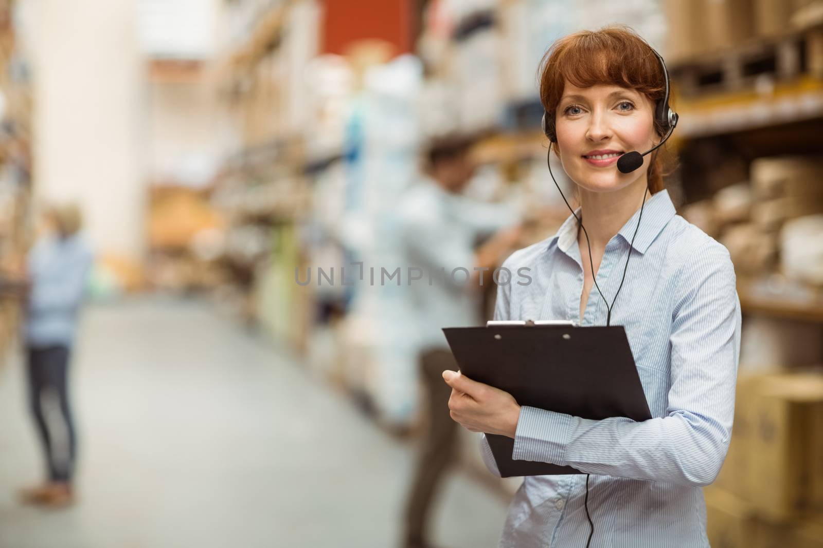Manager wearing a headset while holding clipboard in a large warehouse