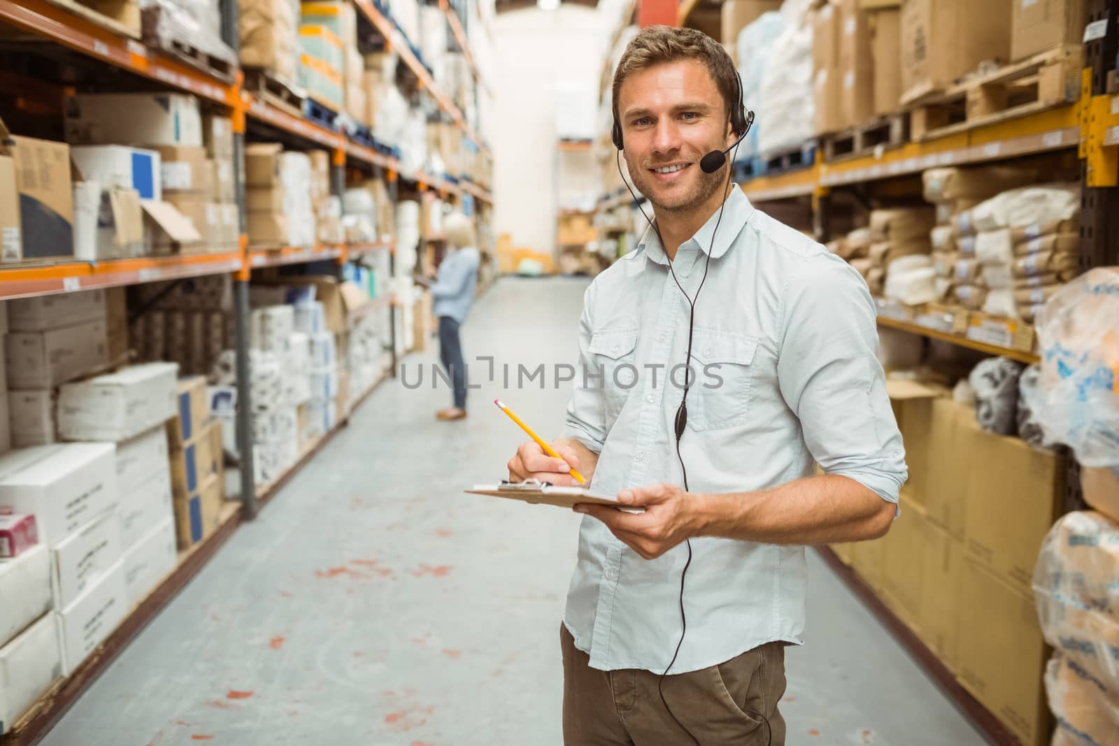 Warehouse manager wearing headset writing on clipboard in a large warehouse