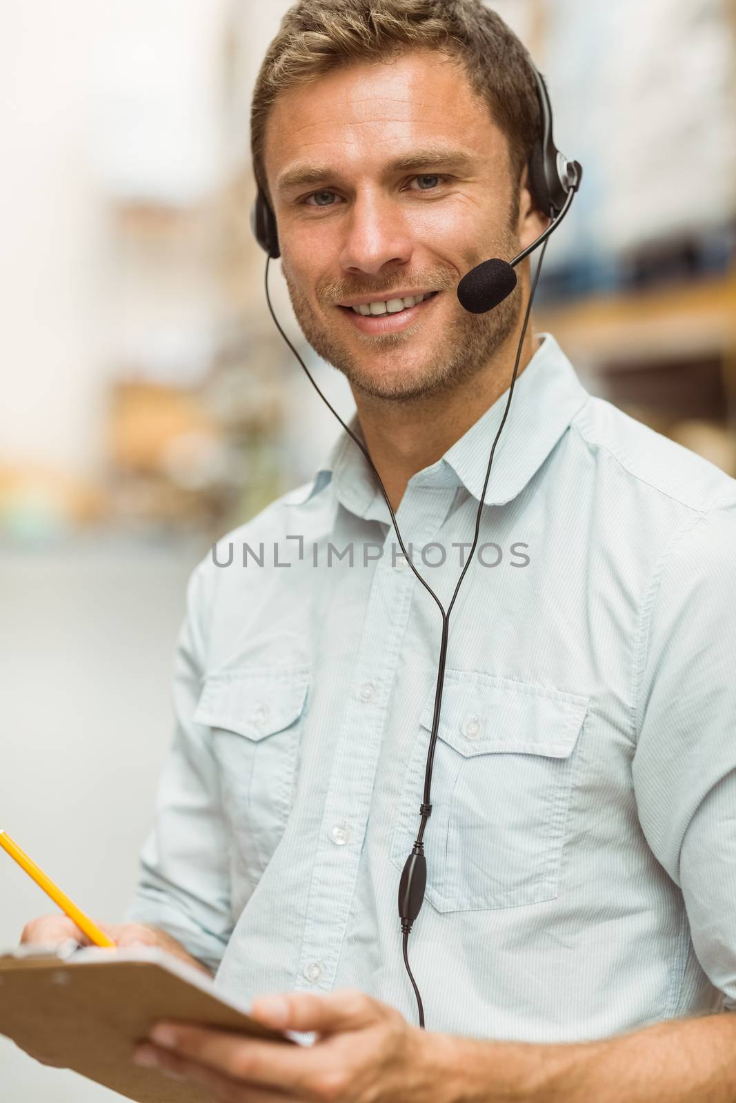 Warehouse manager wearing headset writing on clipboard  by Wavebreakmedia