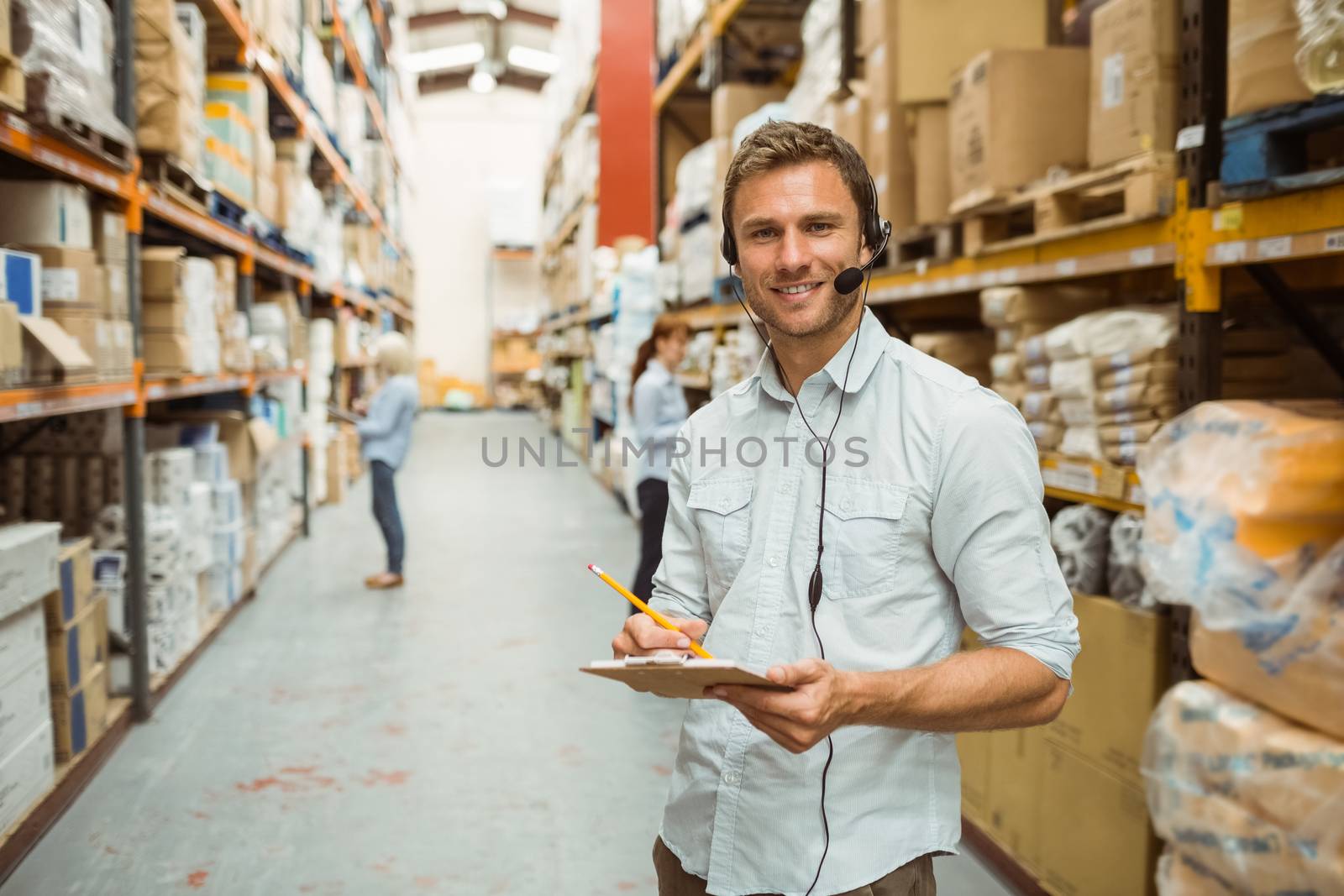 Warehouse manager wearing headset writing on clipboard in a large warehouse