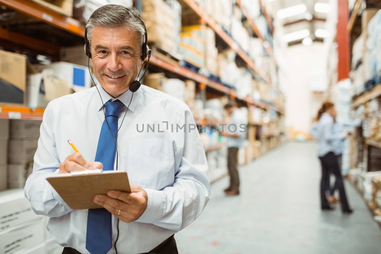 Smiling warehouse manager writing on clipboard in a large warehouse