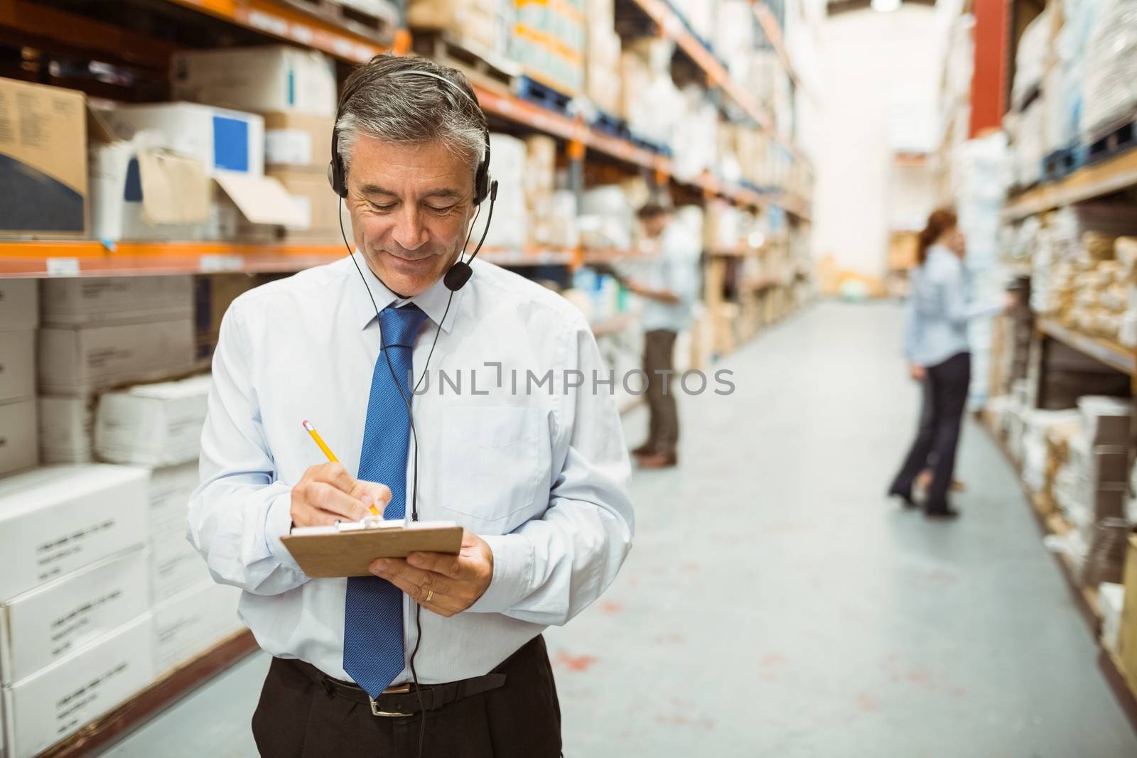 Smiling warehouse manager writing on clipboard in a large warehouse