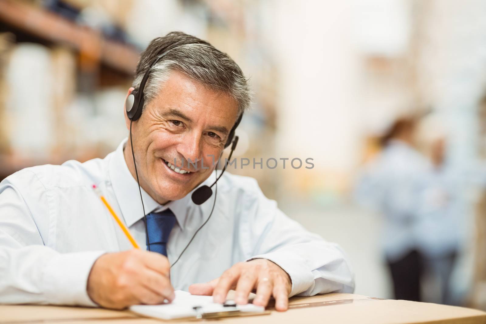 Smiling warehouse manager writing on clipboard in a large warehouse