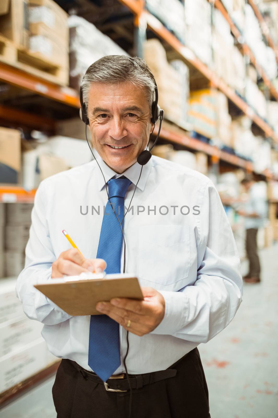 Smiling warehouse manager writing on clipboard in a large warehouse