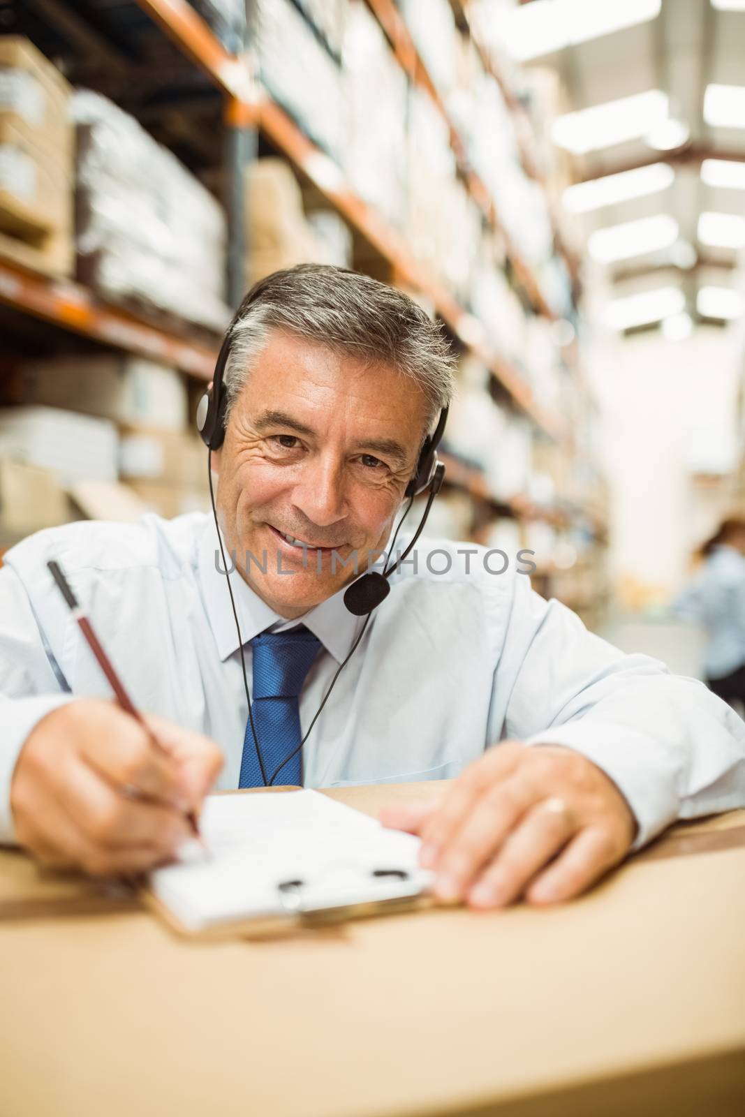 Smiling warehouse manager writing on clipboard in a large warehouse