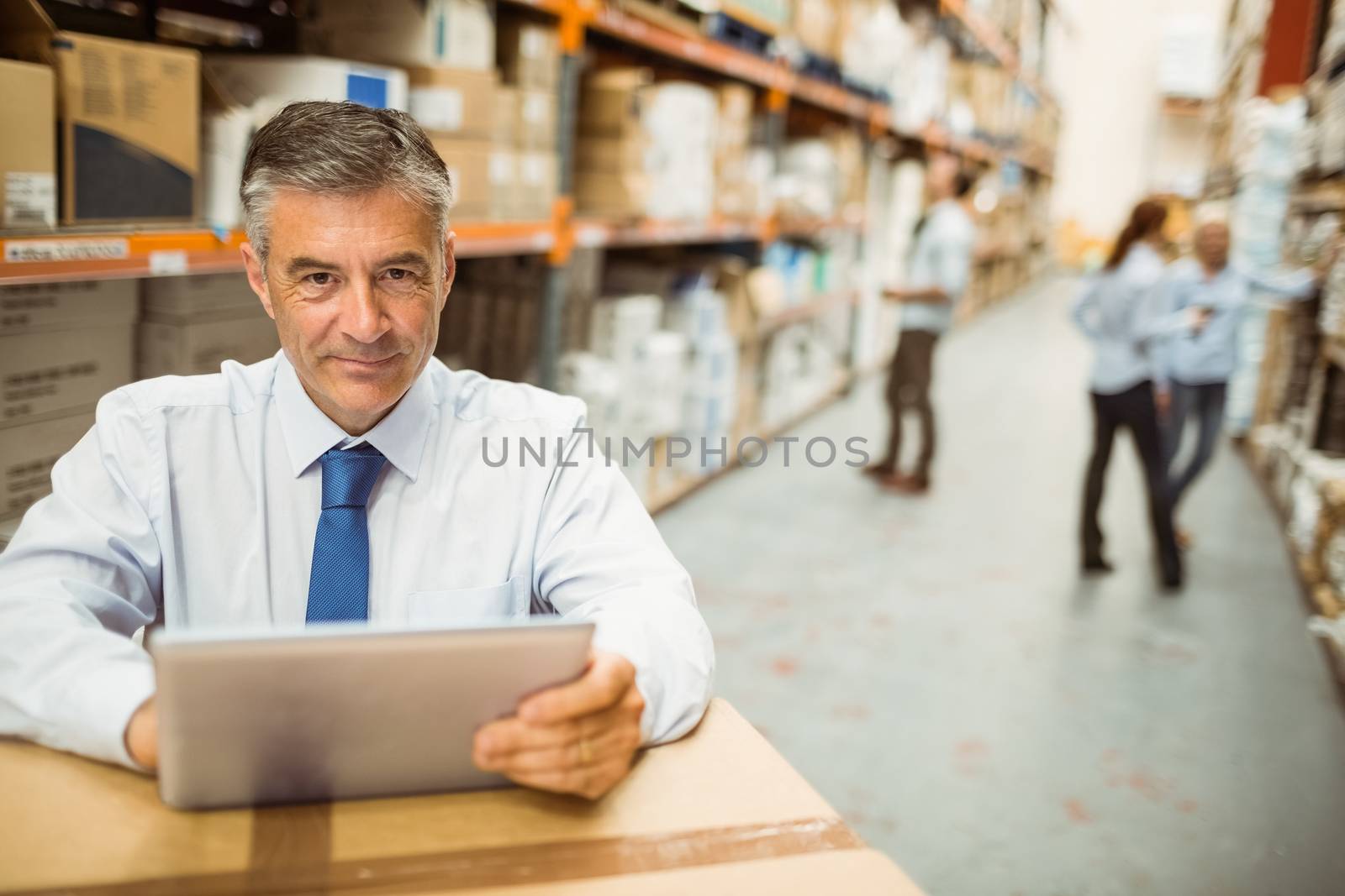 Manager working on tablet pc while looking at camera in a large warehouse