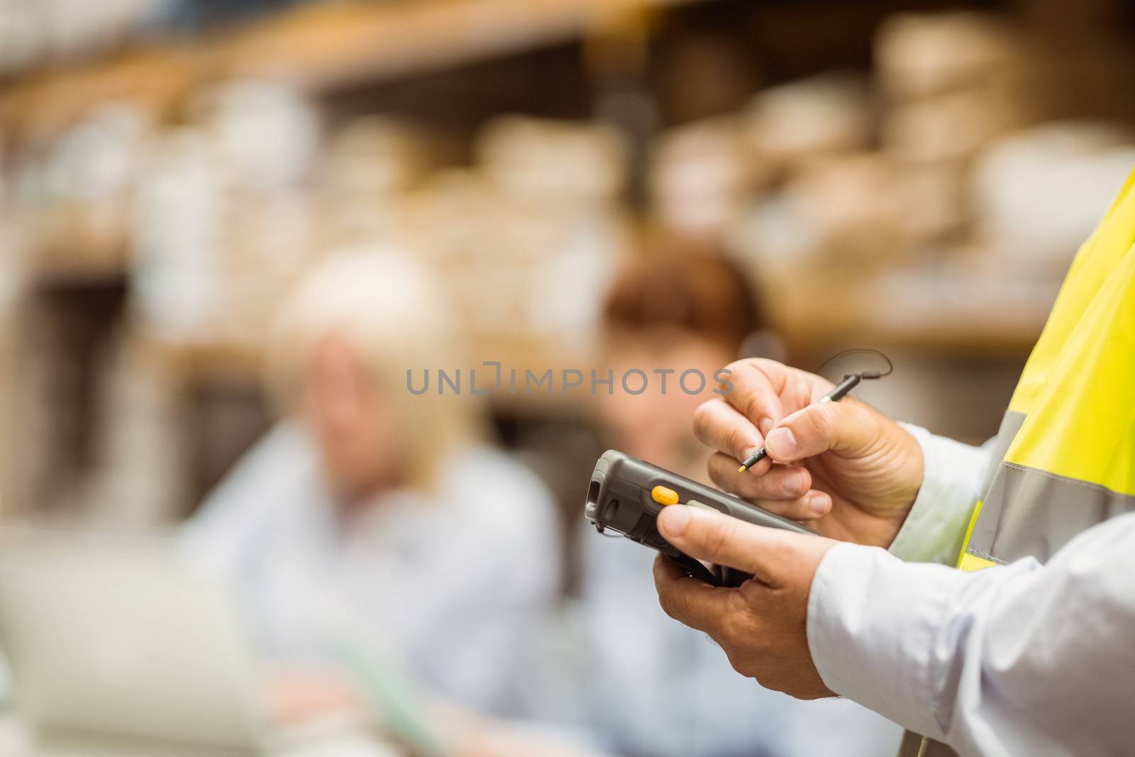 Close up of manager wearing yellow vest using handheld in a large warehouse