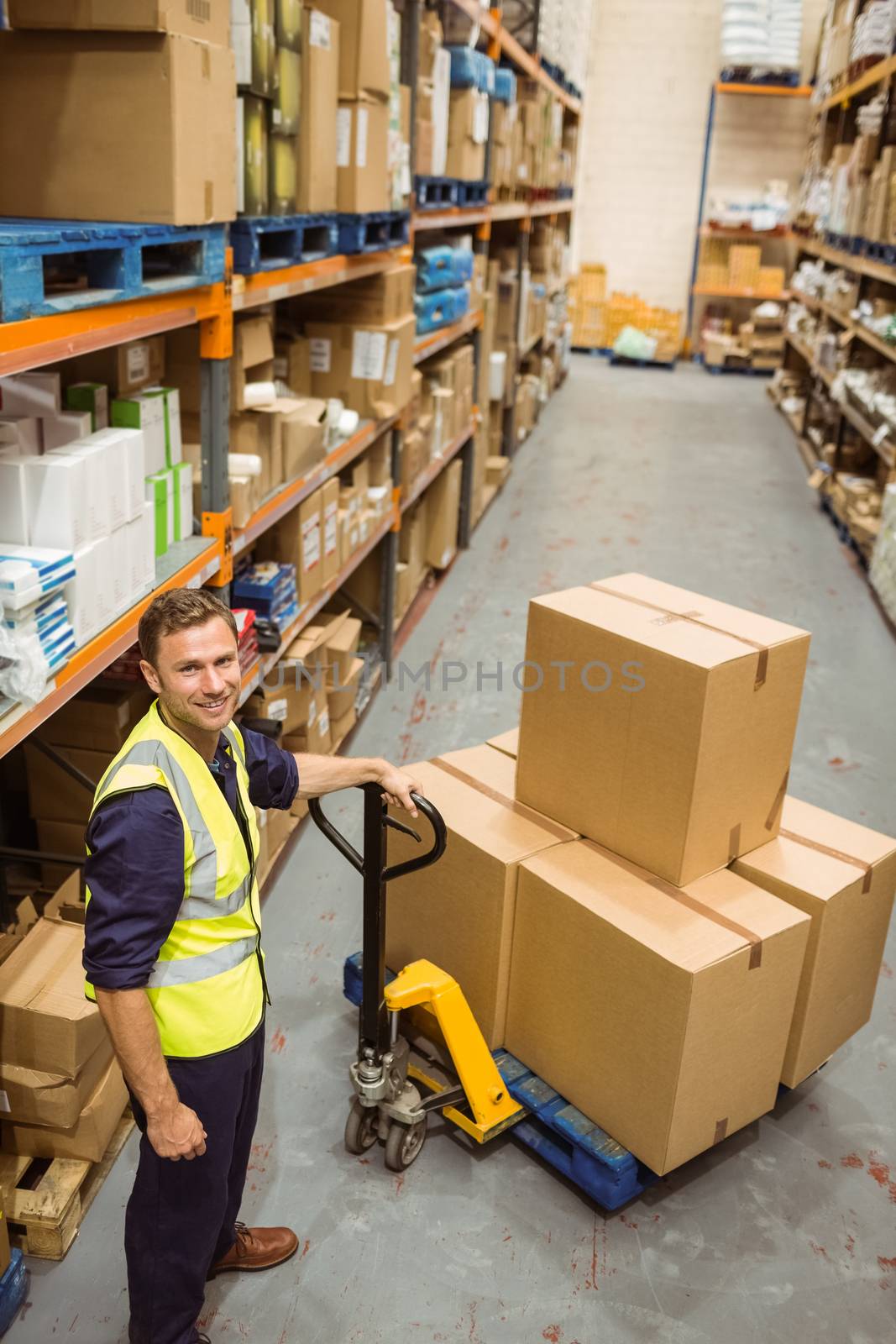 Worker with trolley of boxes smiling at camera in a large warehouse
