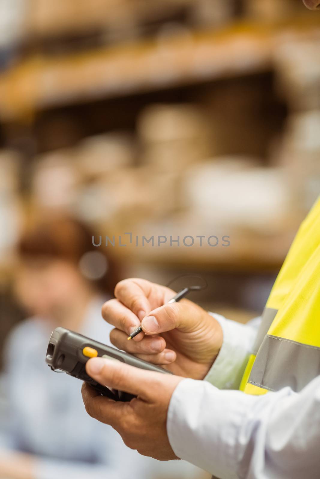 Close up of manager wearing yellow vest using handheld in a large warehouse