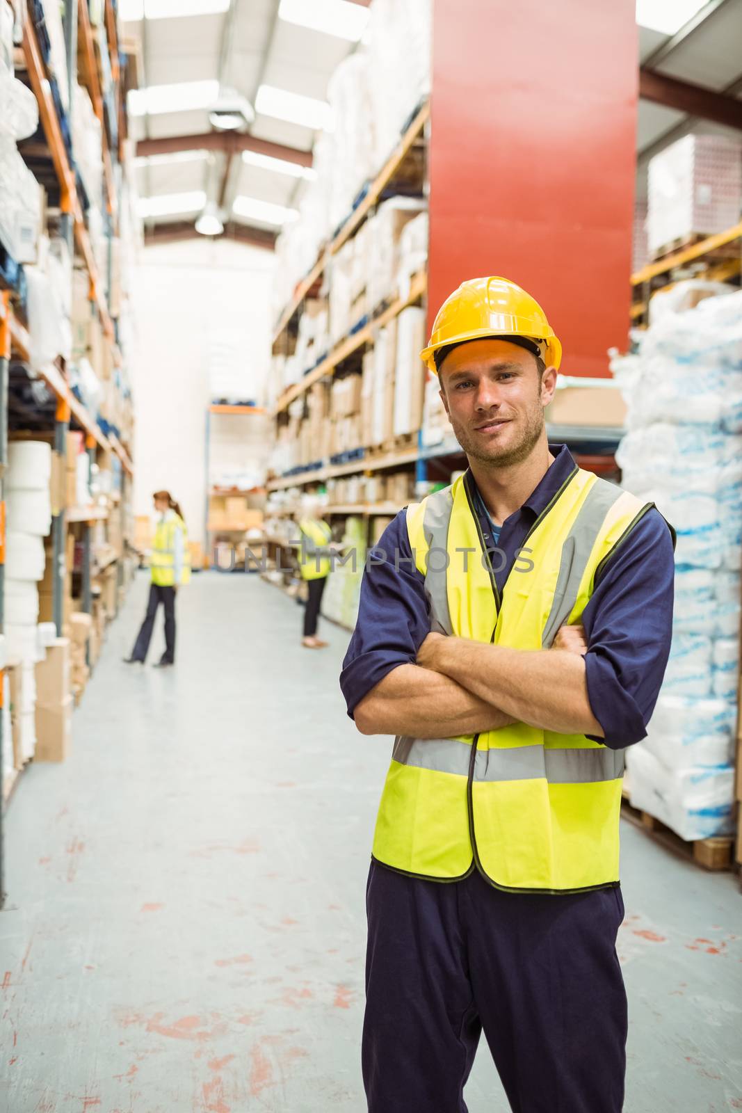Warehouse worker smiling at camera with arms crossed in a large warehouse