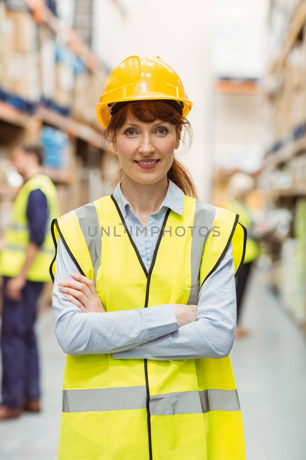 Warehouse manager smiling at camera with arms crossed in a large warehouse