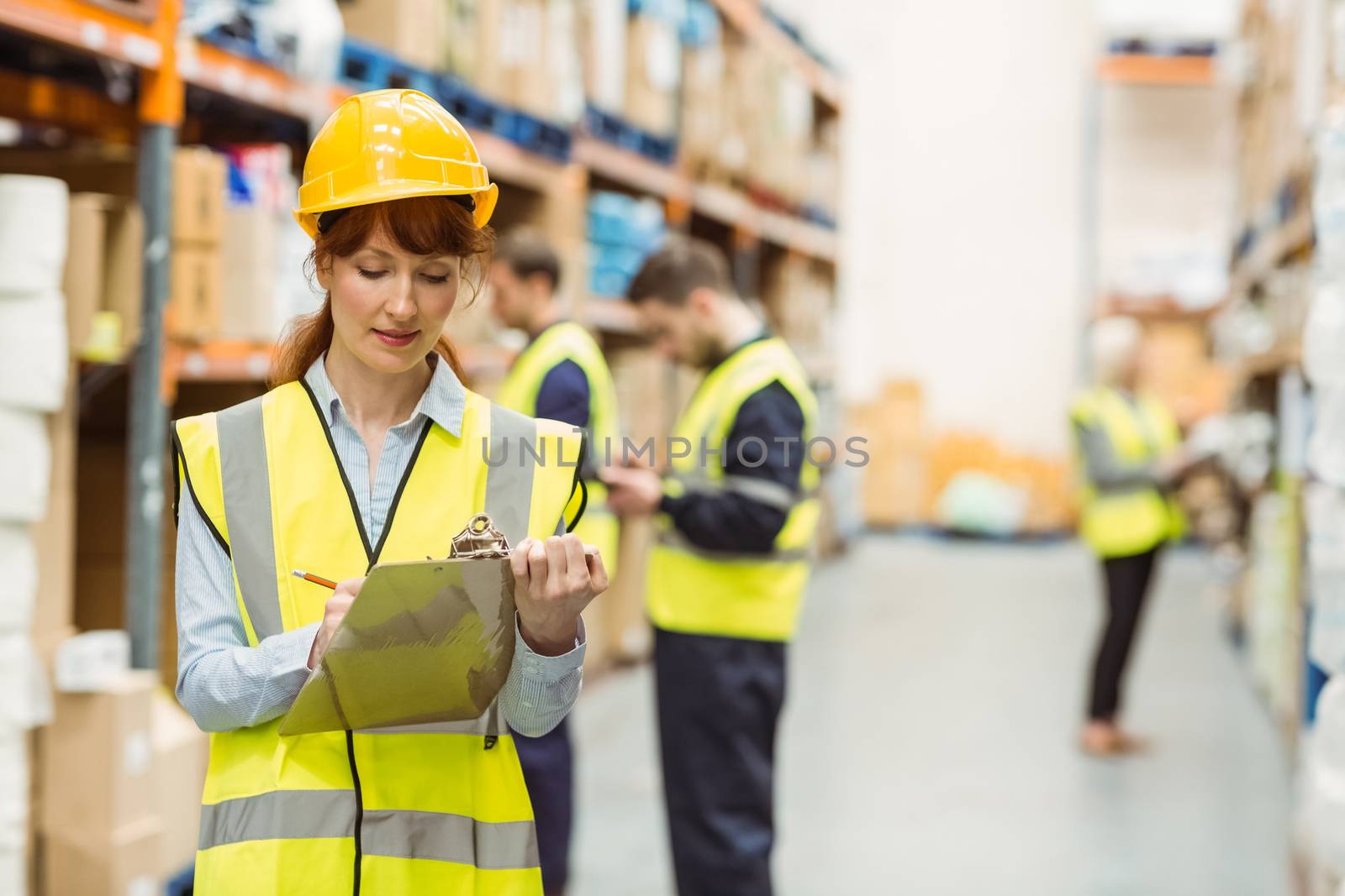 Pretty warehouse manager writing on clipboard by Wavebreakmedia