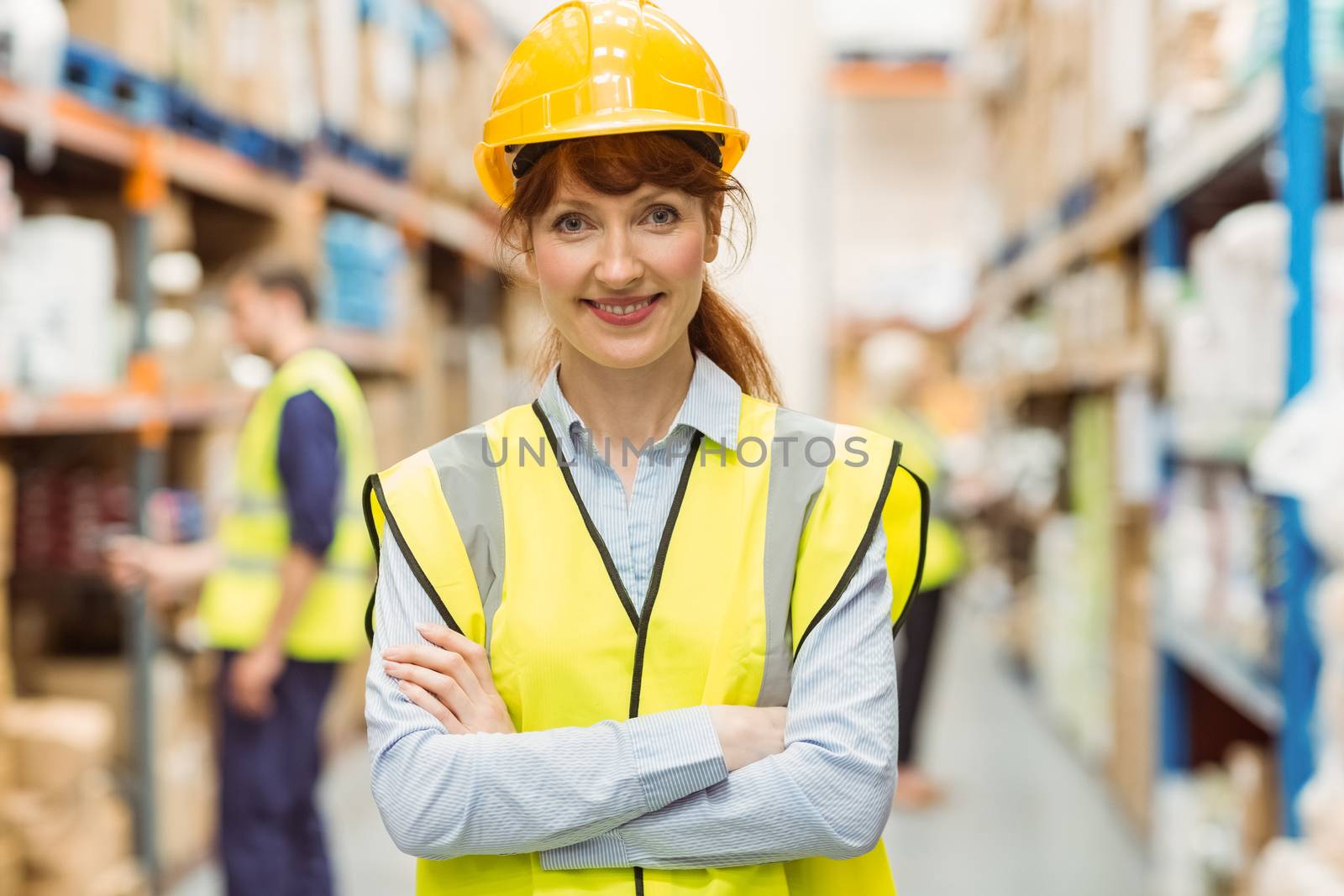 Warehouse manager smiling at camera with arms crossed in a large warehouse