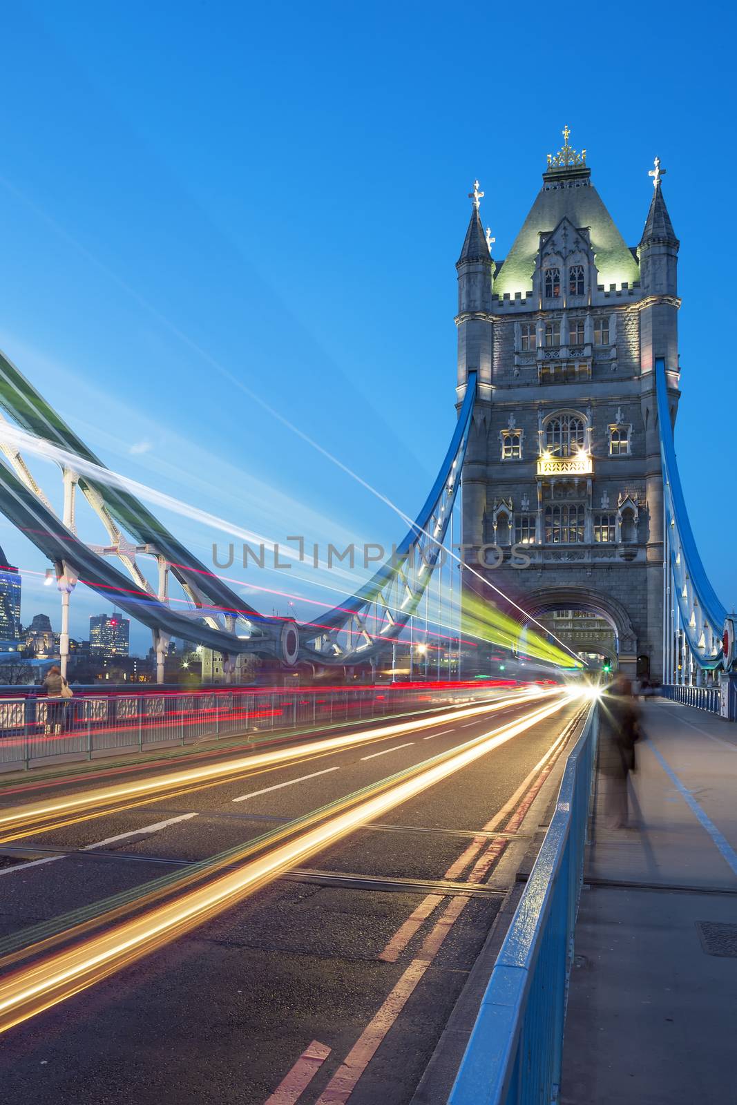 Tower Bridge in London, UK at night with moving red double-decker bus leaving light traces