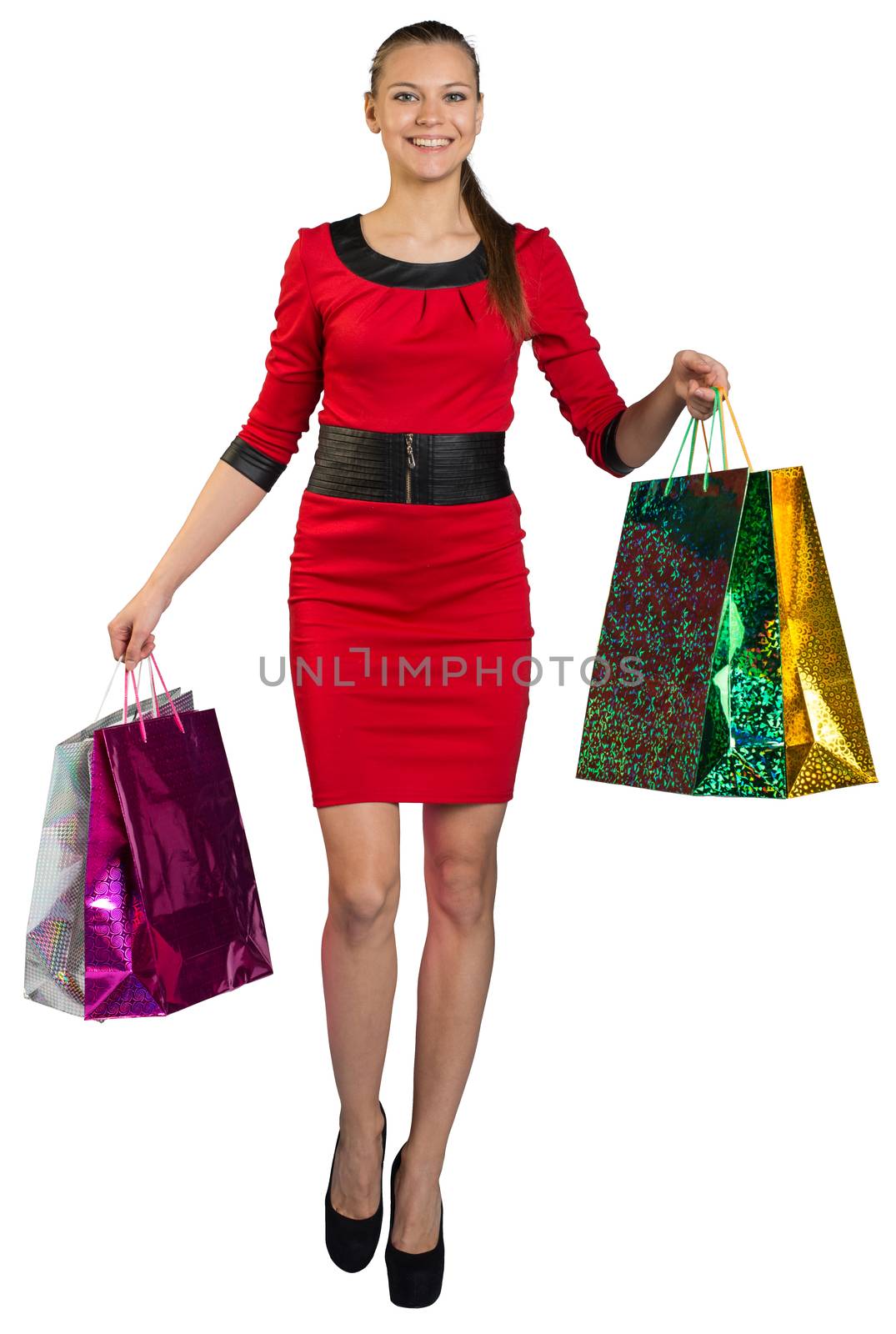Walking young woman with teeth smile and right leg forward, handing colorful shopping bags up and looking at camera. Isolated background