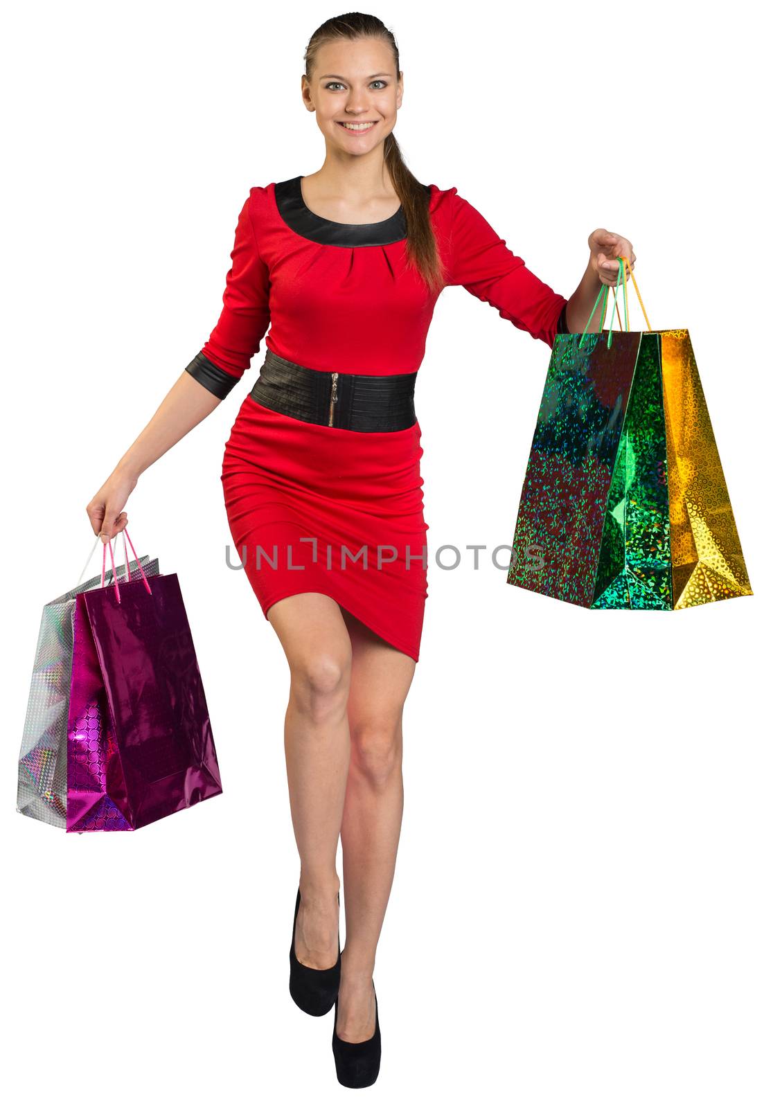 Walking young woman with teeth smile and right leg forward, handing four colorful shopping bags up and looking at camera. Isolated background