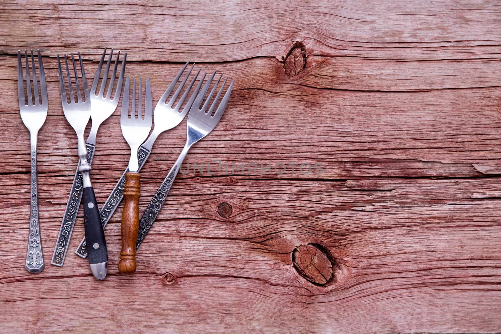 Random pile of assorted rustic forks arranged on the side of a rustic wooden table with copyspace in a concept of country cuisine, overhead view