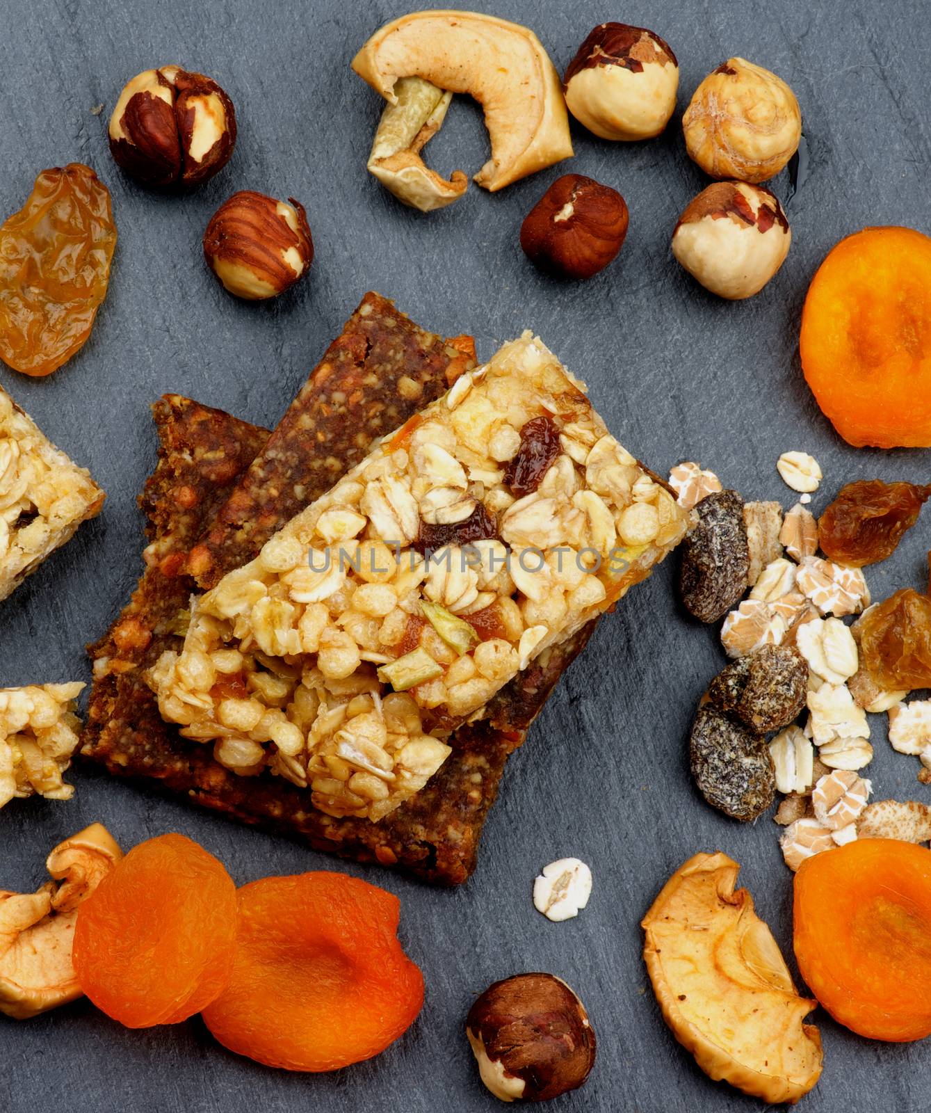 Stack of Useful Granola Bars with Muesli, Nuts and Dried Apricots closeup on Black Stone background. Top View