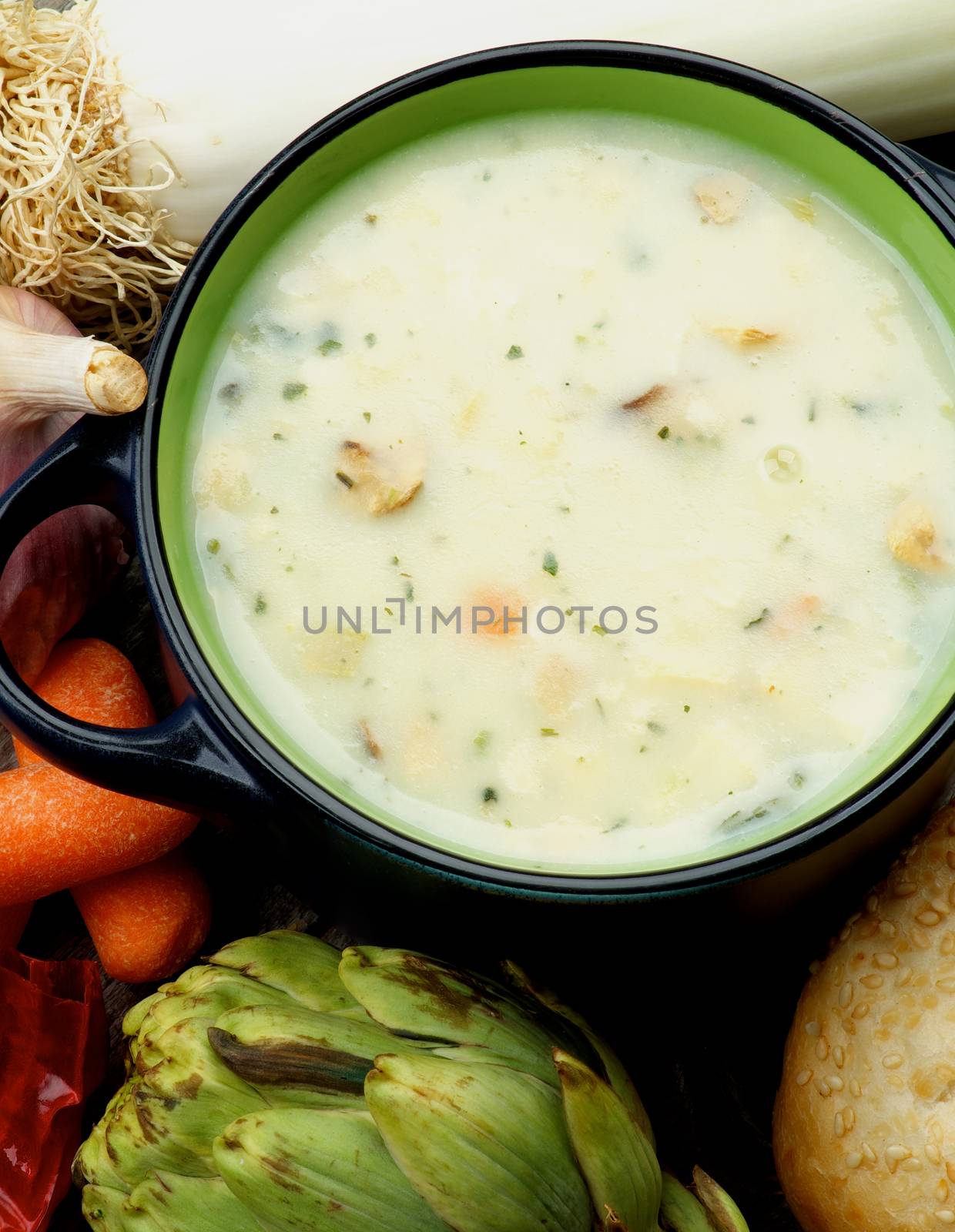 Healthy Artichoke Creamy Soup with Raw Leek, Carrot, Garlic and Cheese in Dark Blue Pannikin closeup. Top View