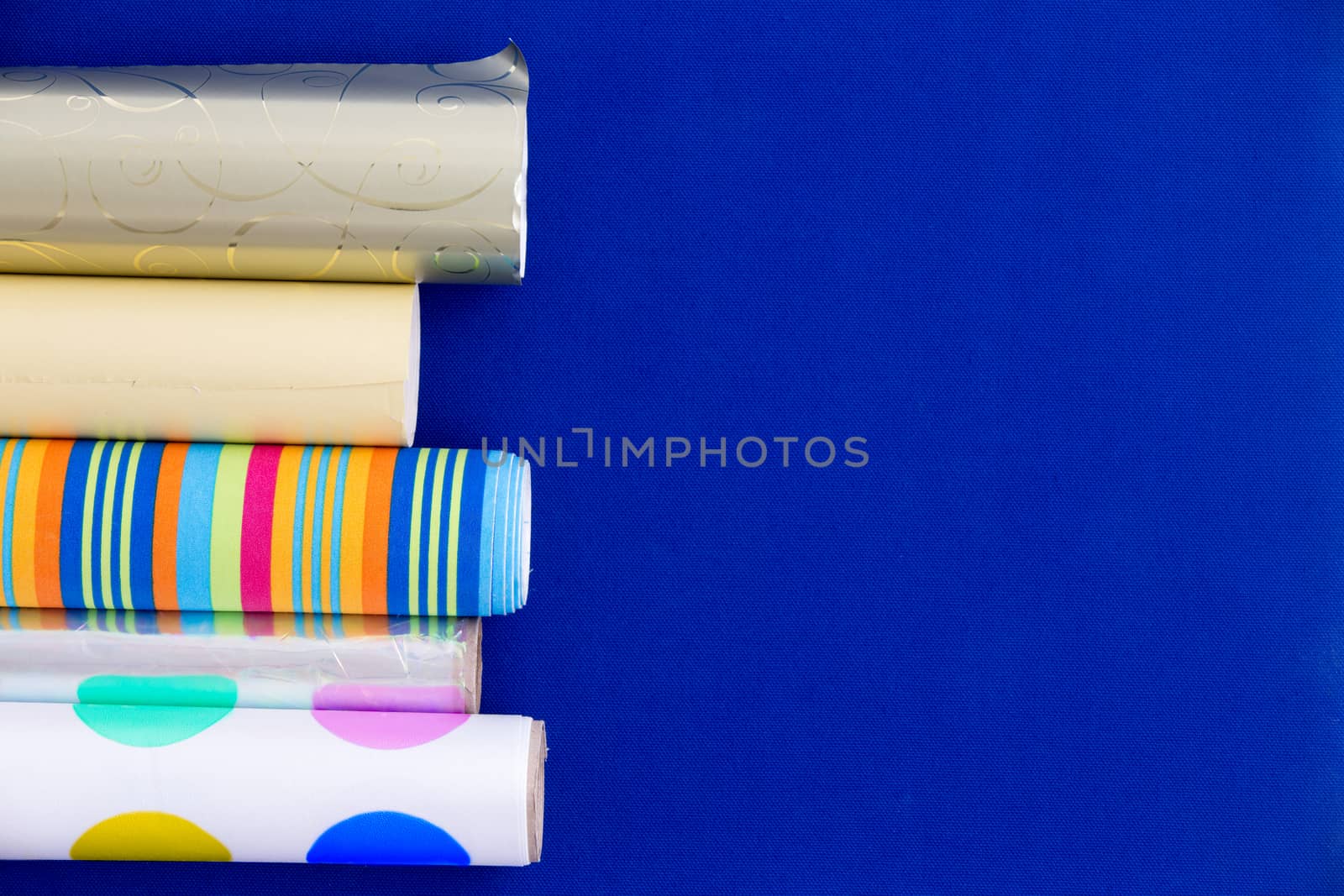 Colorful rolls of patterned and metallic wrapping paper arranged as a side border over a blue background with copyspace