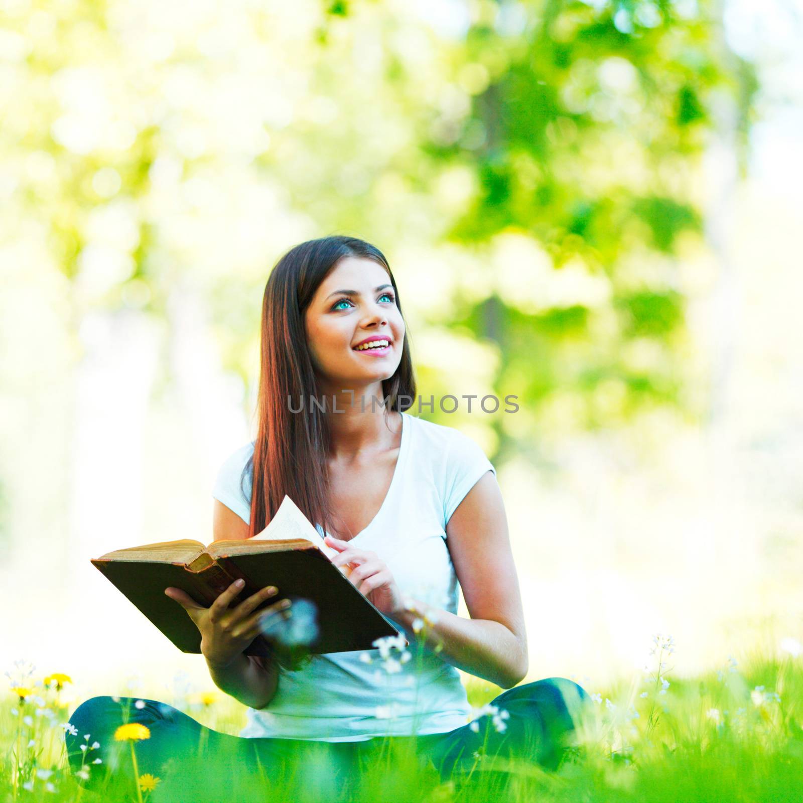 Young beautiful woman with book resting on fresh green grass with flowers