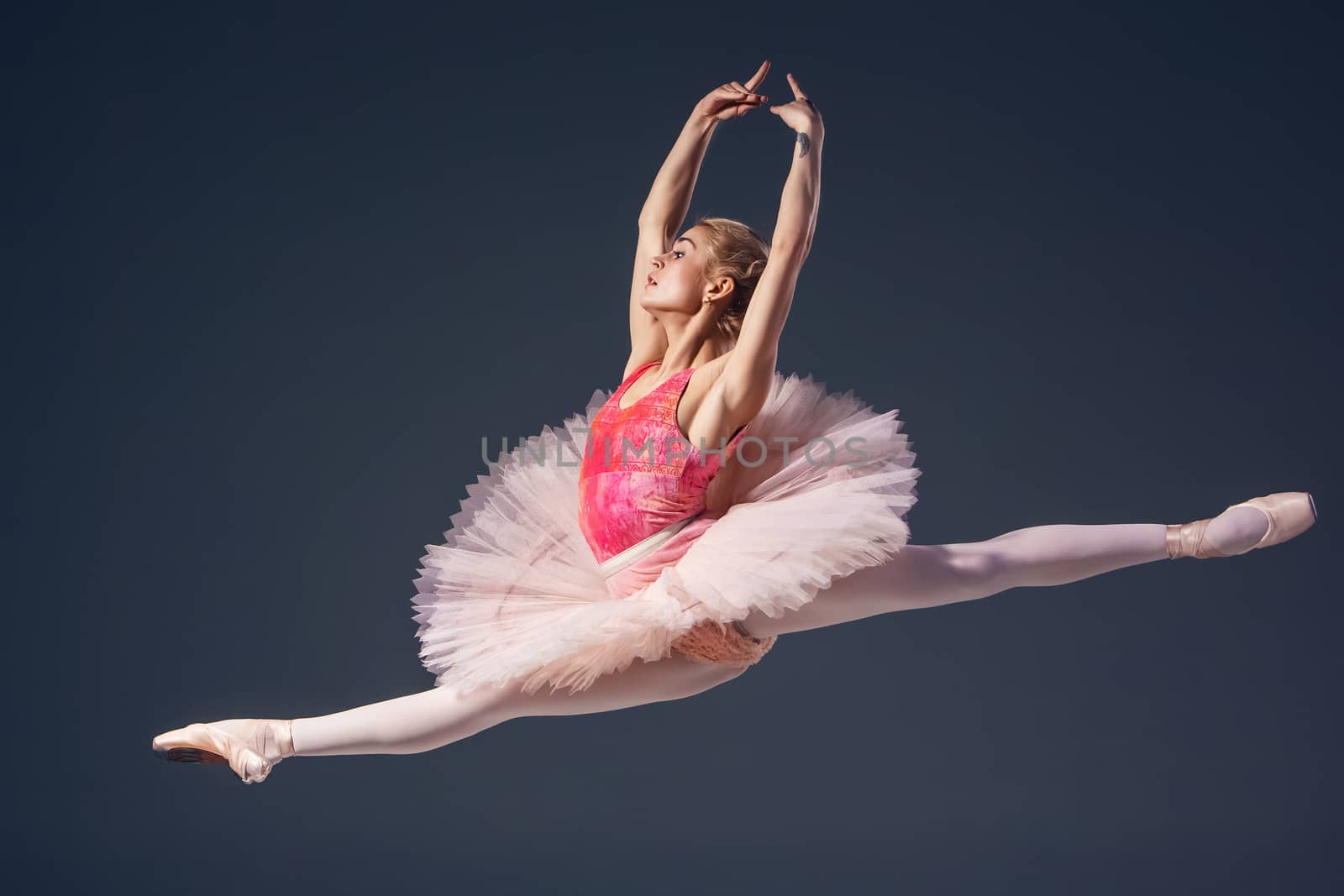 Beautiful female ballet dancer on a grey background. Ballerina is wearing  pink tutu and pointe shoes