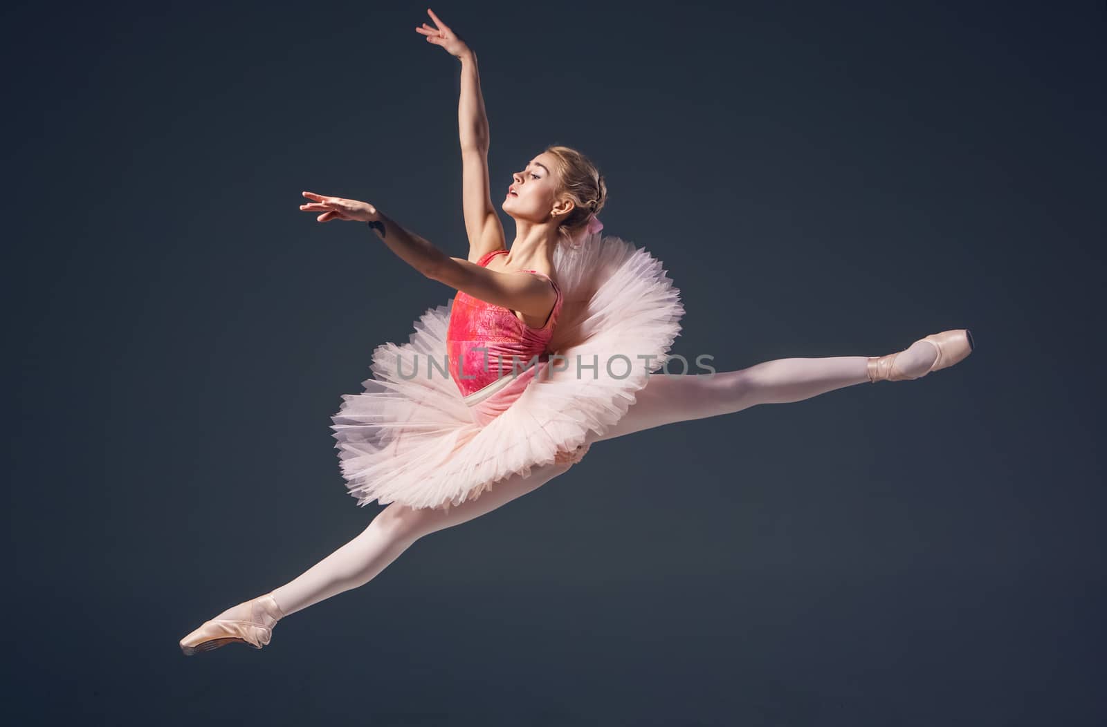 Beautiful female ballet dancer on a grey background. Ballerina is wearing  pink tutu and pointe shoes