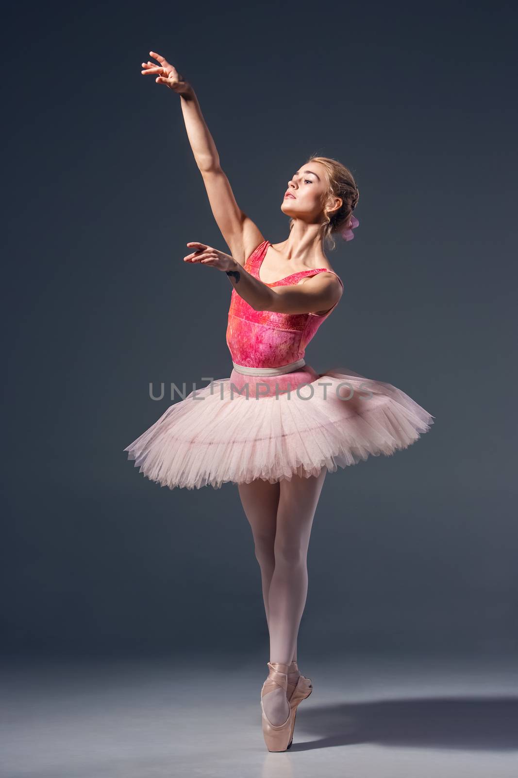 Portrait of the ballerina in ballet pose on a grey background. Ballerina is wearing  pink tutu and pointe shoes