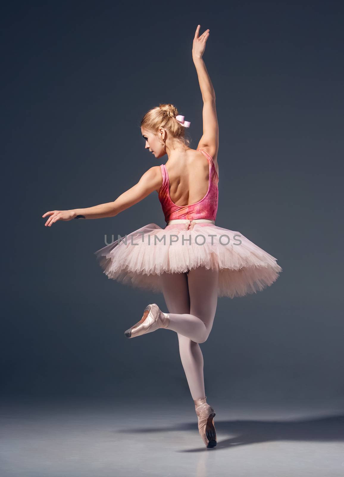 Portrait of the ballerina in ballet pose on a grey background. Ballerina is wearing  pink tutu and pointe shoes