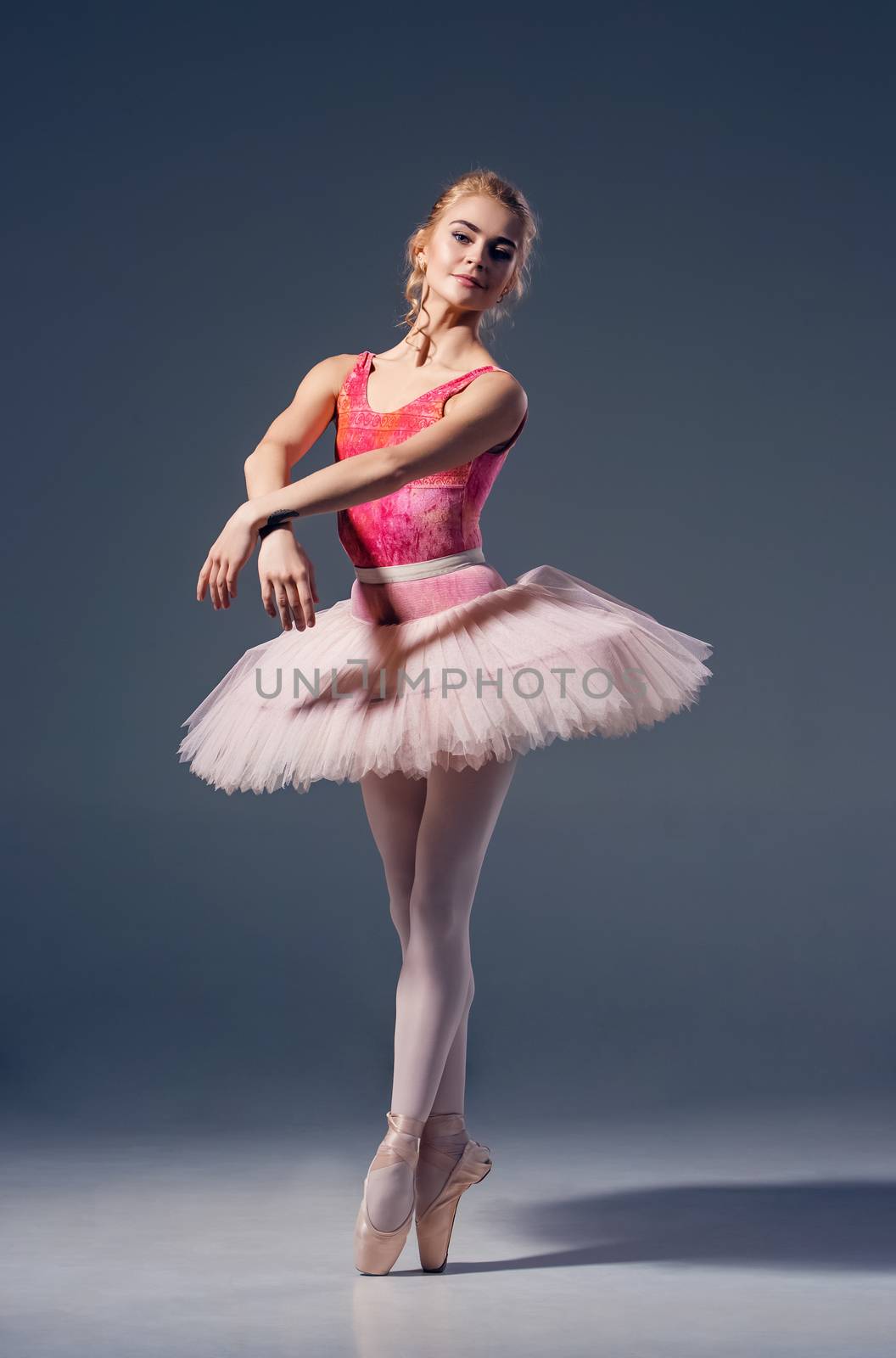 Portrait of the ballerina in ballet pose on a grey background. Ballerina is wearing  pink tutu and pointe shoes