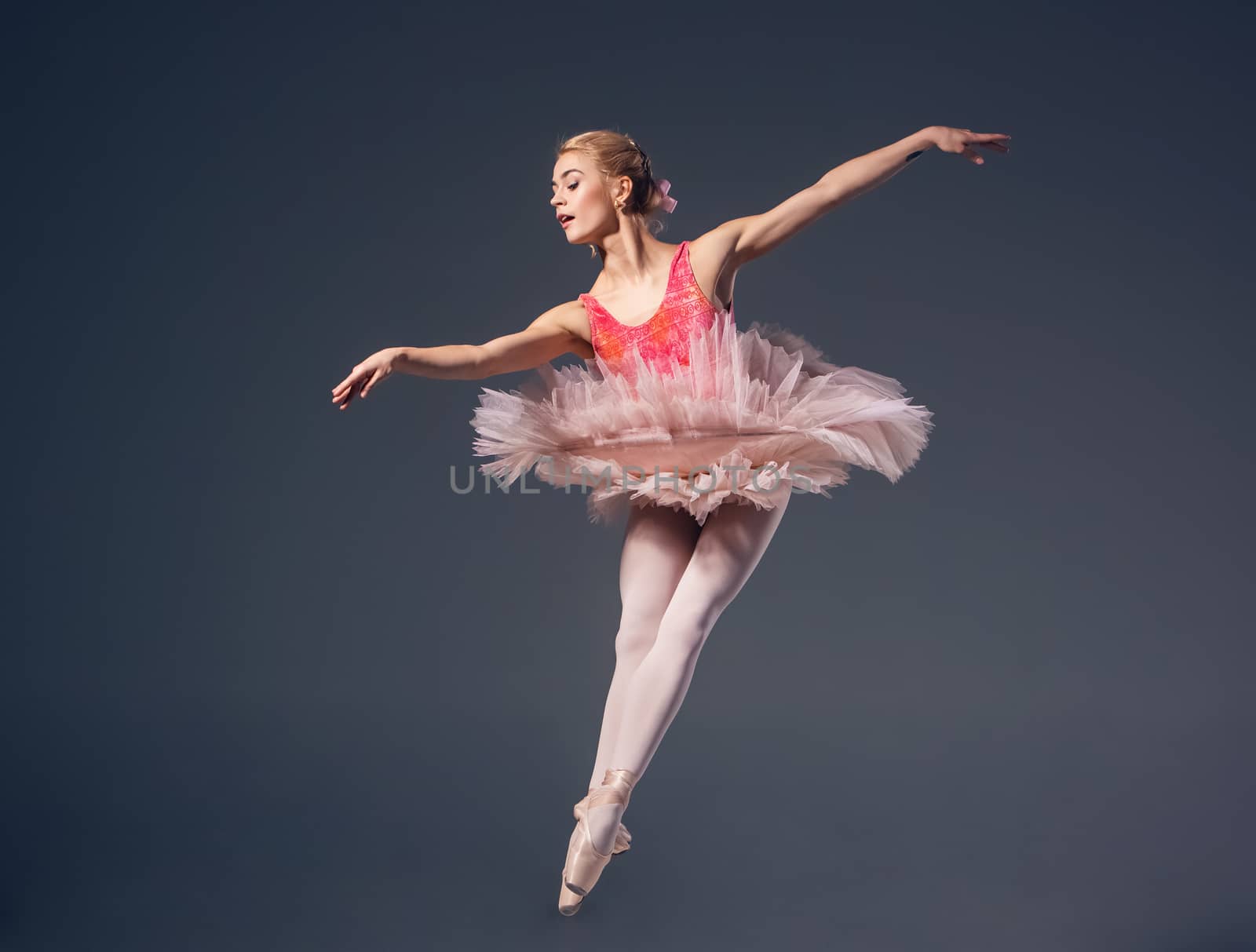 Beautiful female ballet dancer on a grey background. Ballerina is wearing  pink tutu and pointe shoes