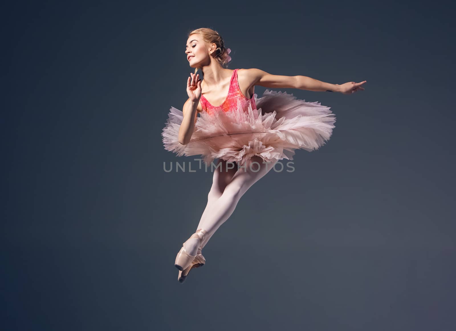 Beautiful female ballet dancer on a grey background. Ballerina is wearing  pink tutu and pointe shoes