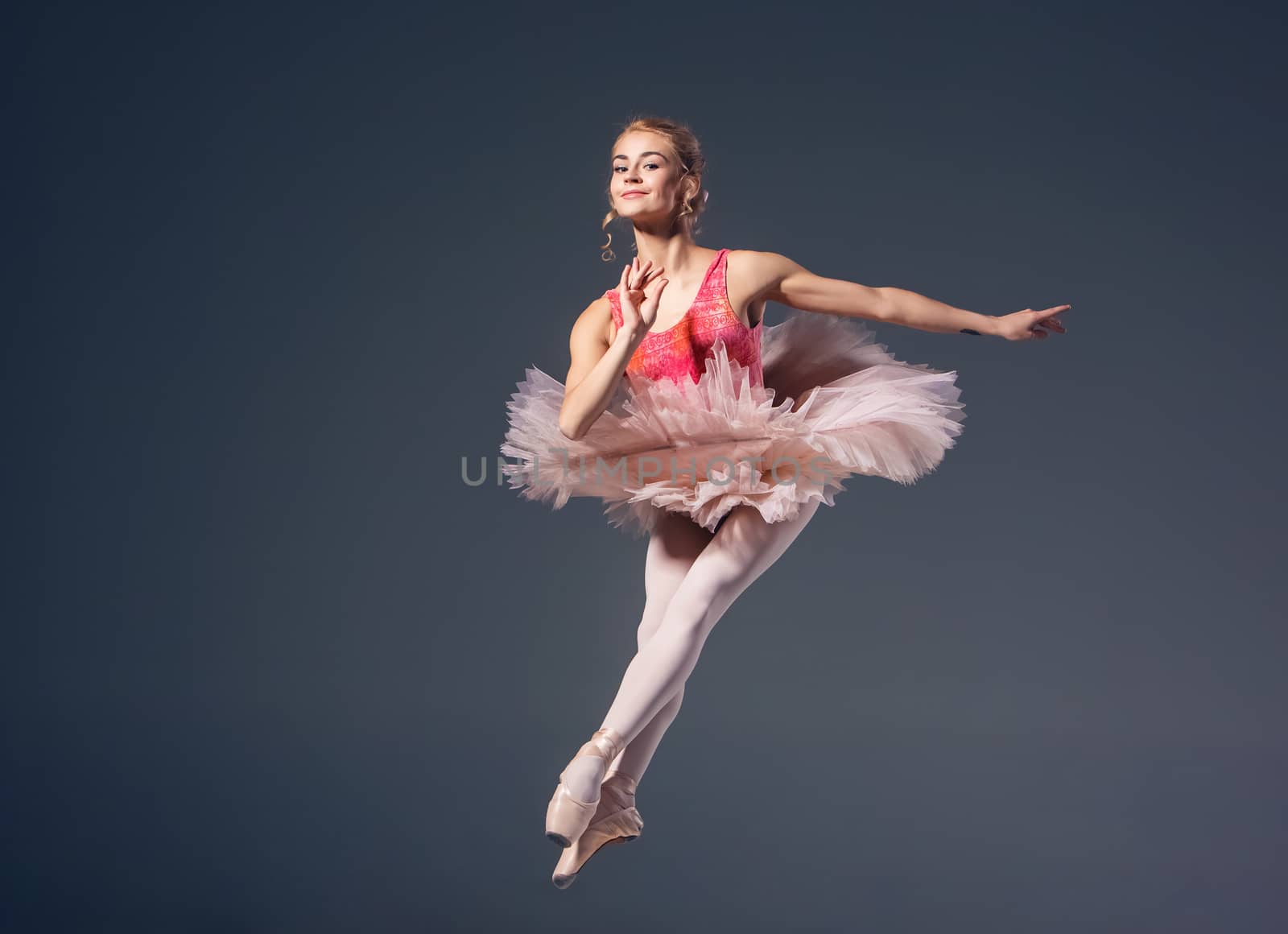 Beautiful female ballet dancer on a grey background. Ballerina is wearing  pink tutu and pointe shoes