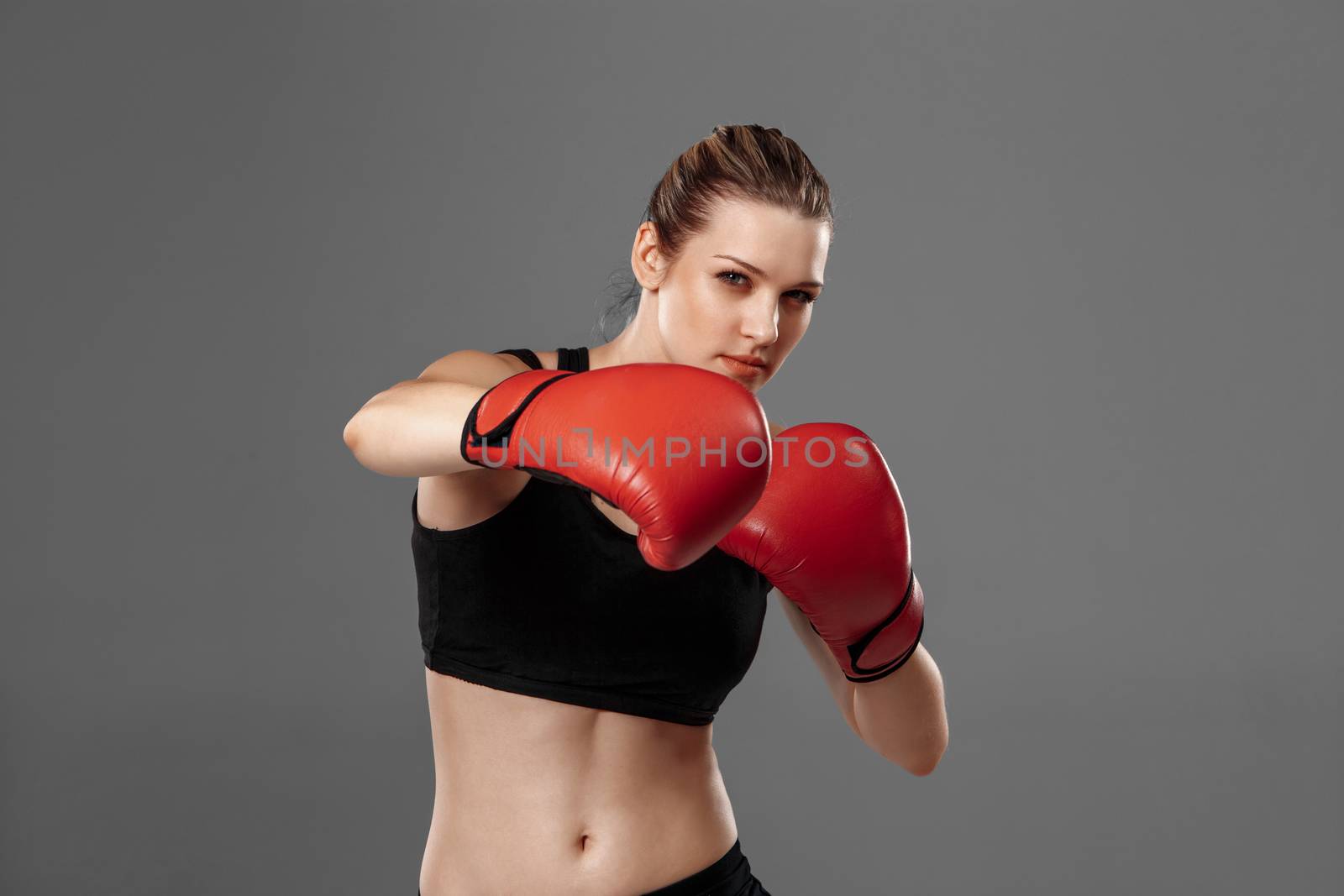 beautiful woman with the red gloves is boxing on gray background