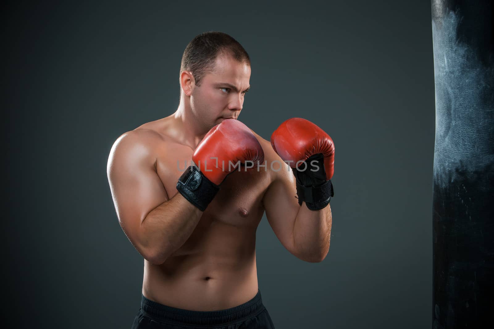 Young boxer in red gloves boxing over black background