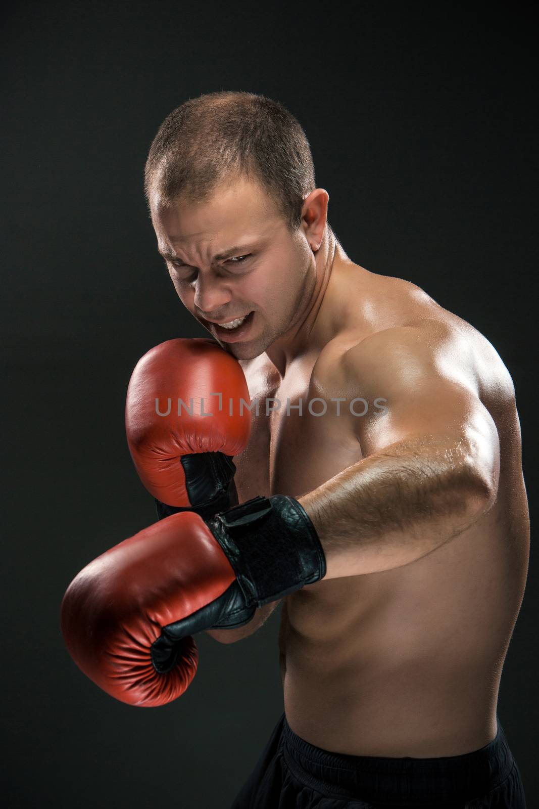 Young boxer in red gloves boxing over black background