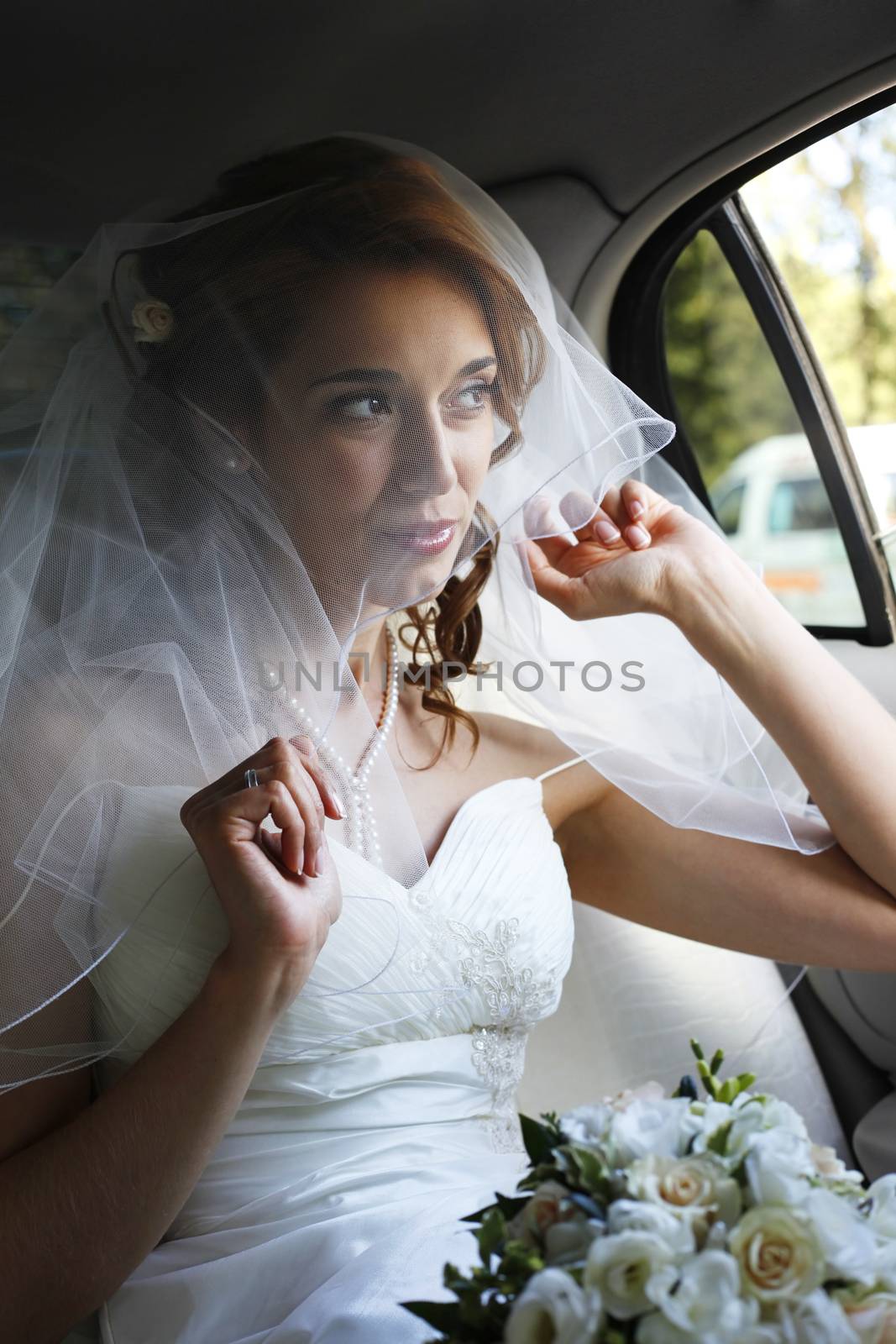Beautiful bride with wedding bouquet in white car