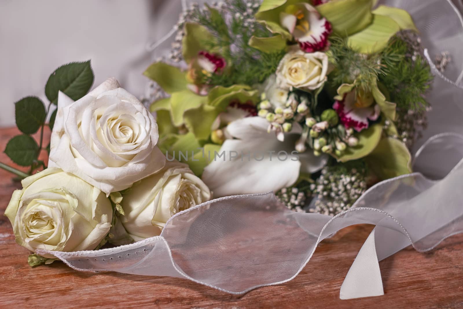 three white roses and bouquets of flowers on an old wooden base