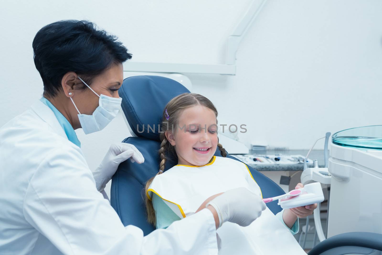 Female dentist teaching girl how to brush teeth by Wavebreakmedia